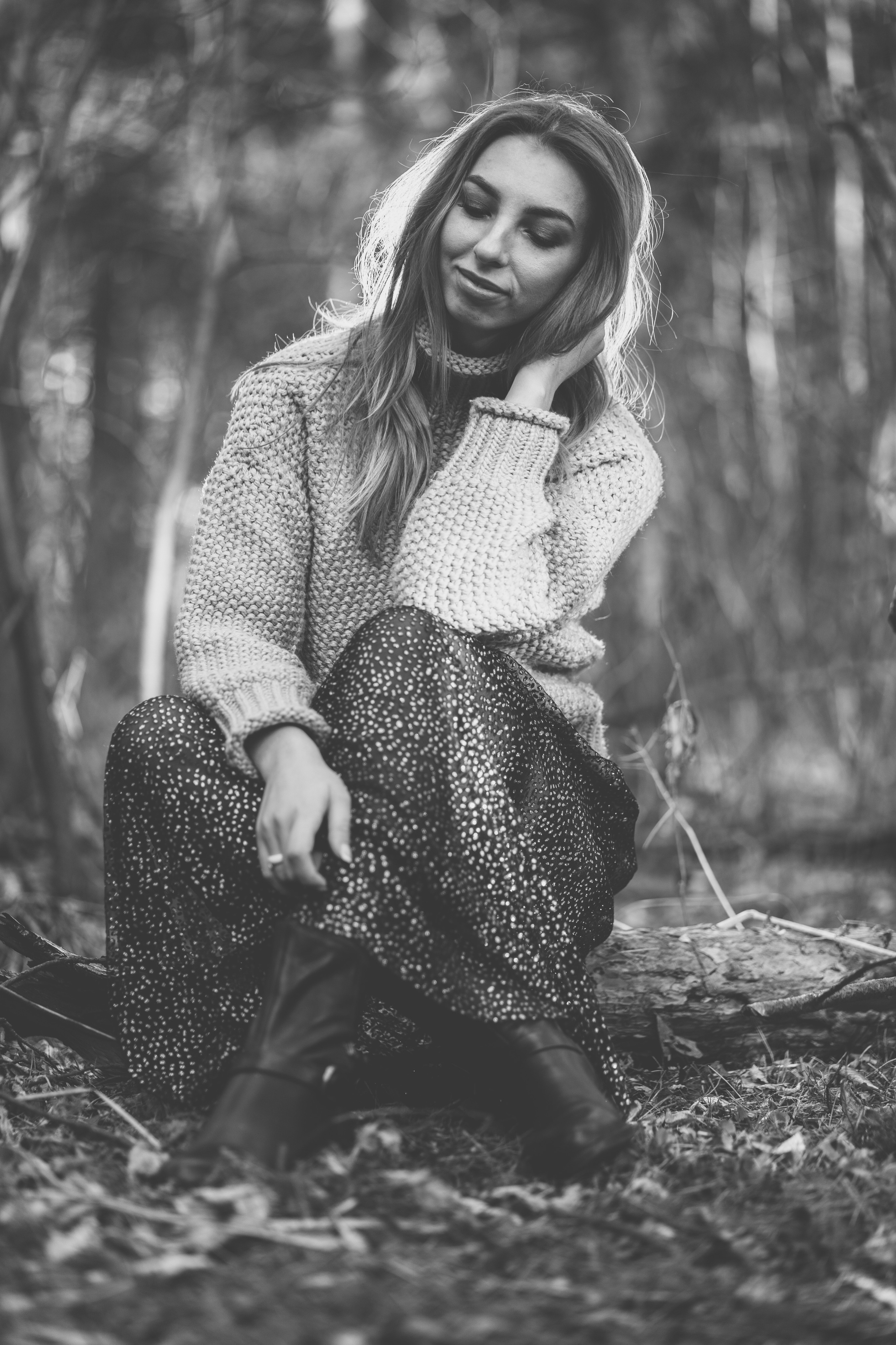 Девушка в вязанном свитере с горлом и легком платье, сидит на бреве и загадочно улыбается