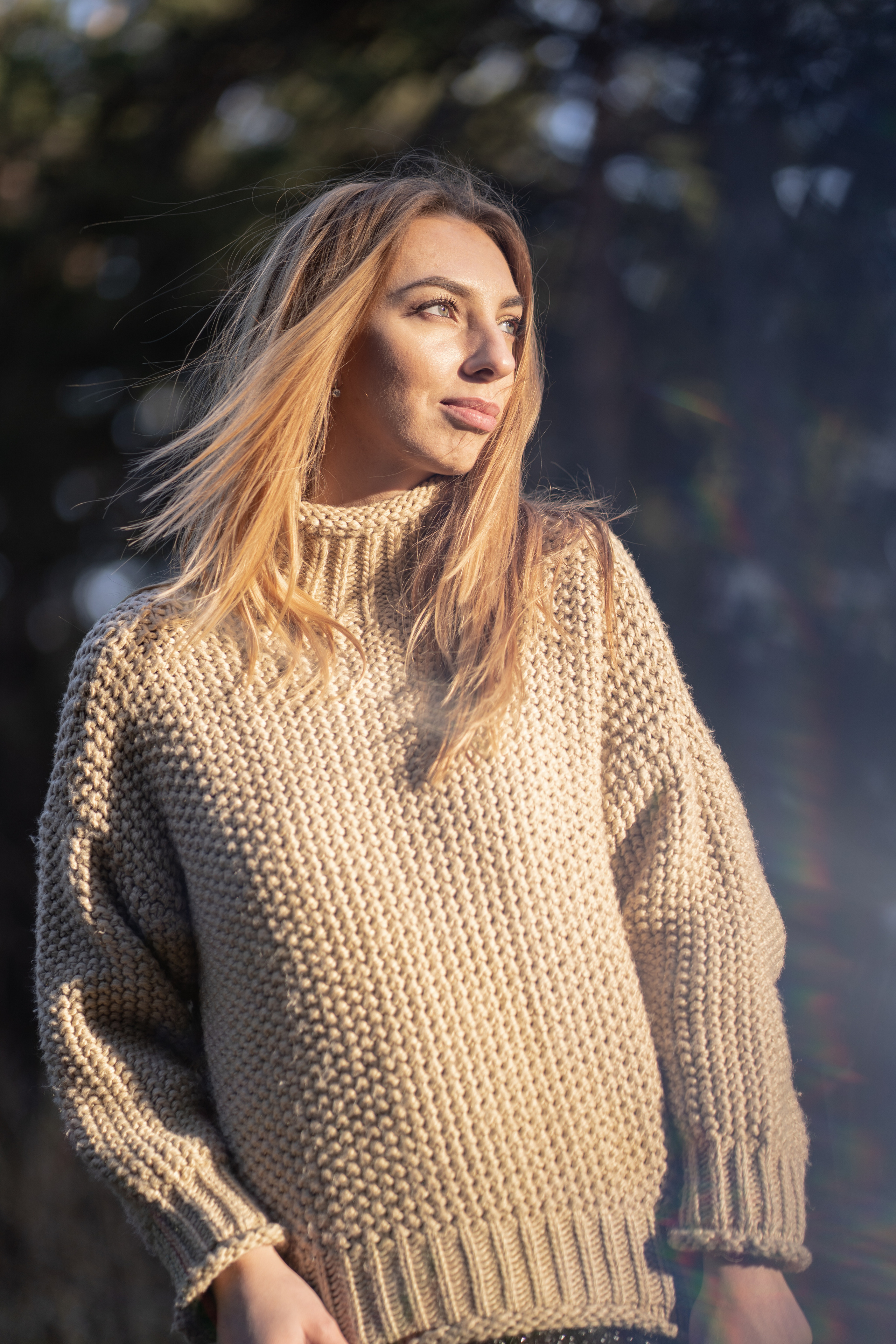 Девушка в вязанном свитере с горлом, мило улыбается и смотрит не в камеру