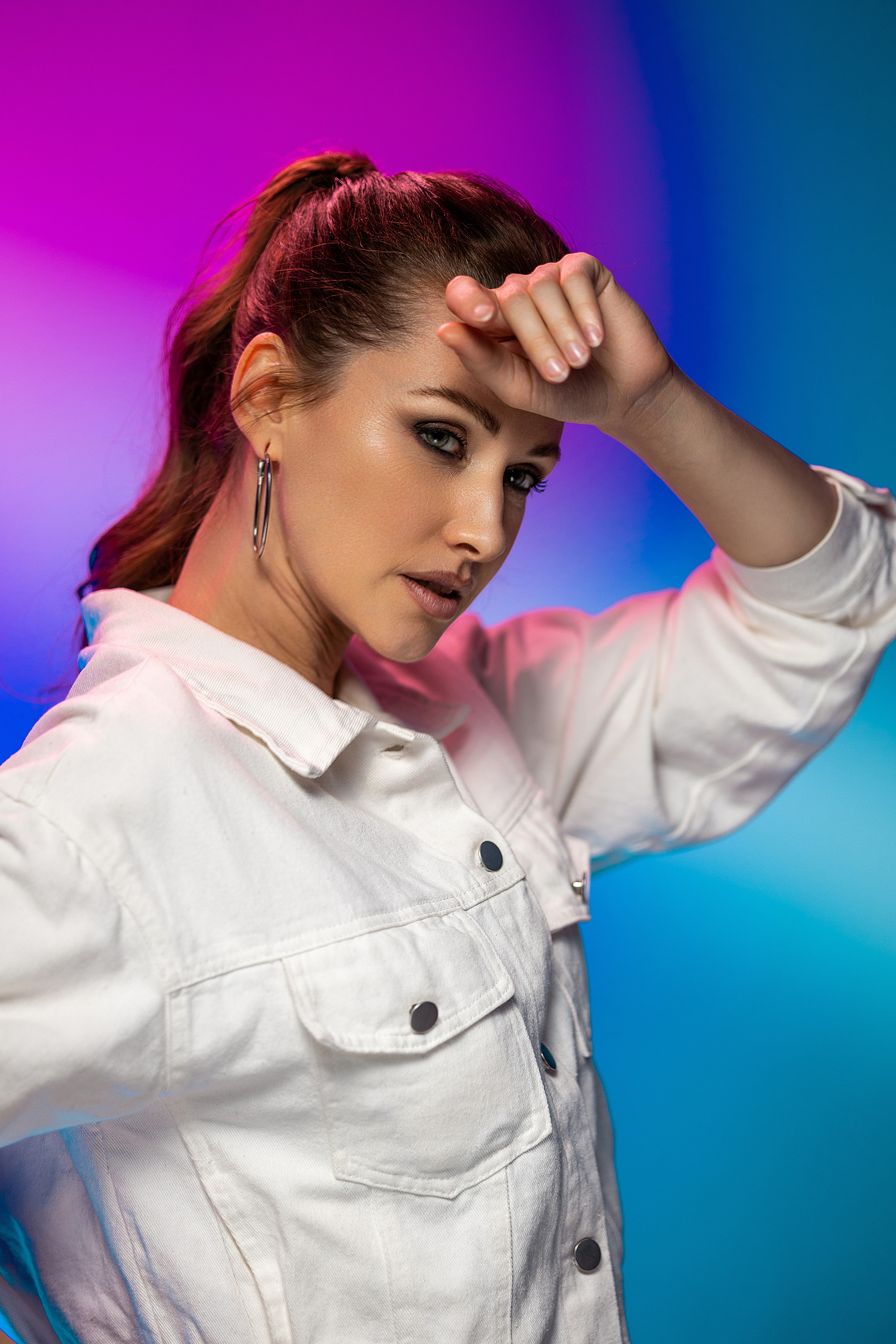 Девушка модельной внешности в белой джинсовой куртке на фиолетово-голубом фоне