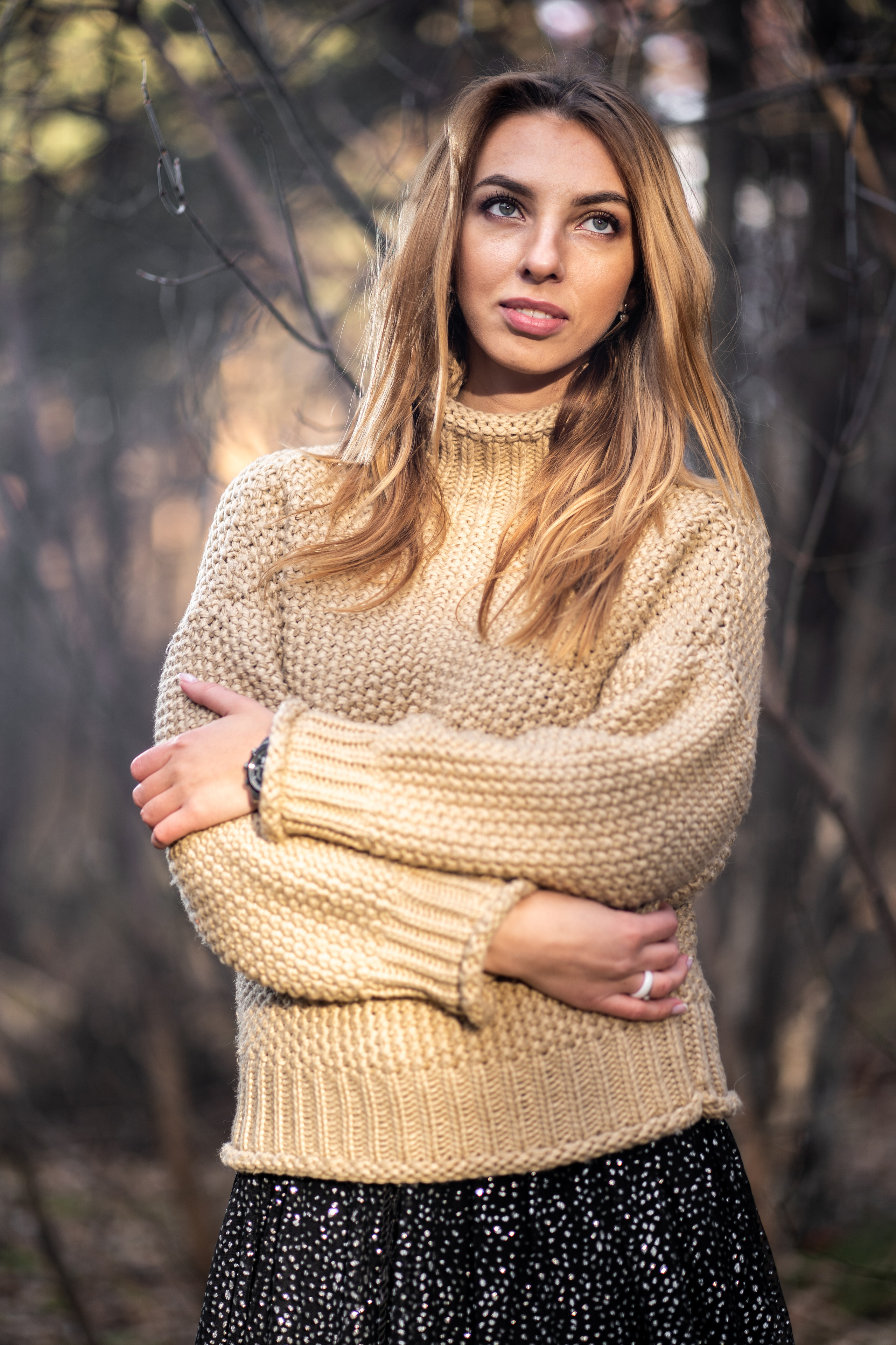 Девушка в вязанном свитере с горлом и легком платье,  мило улыбается и смотрит не в камеру