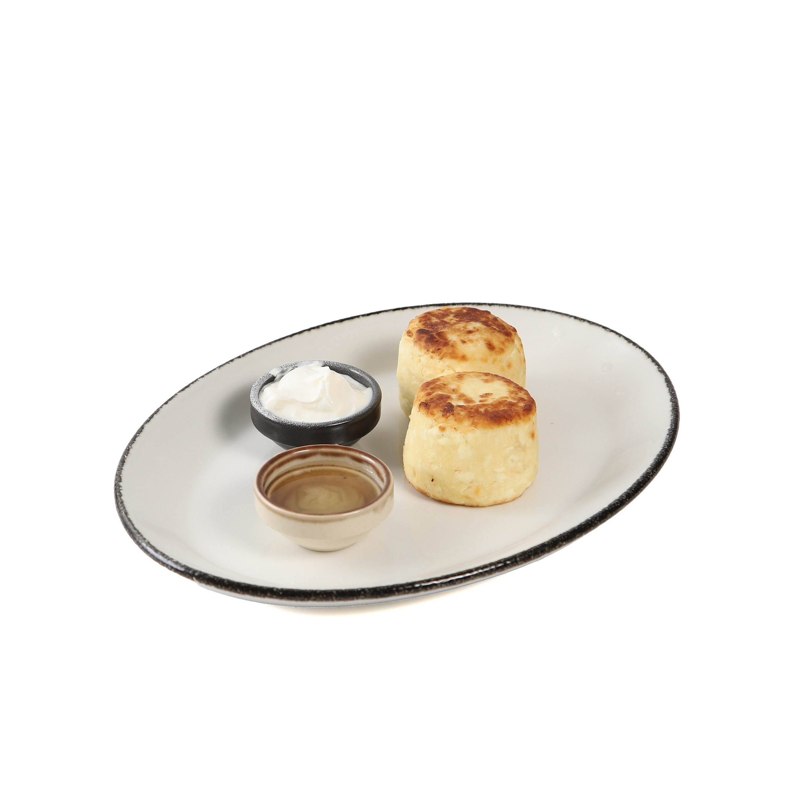 Фуд-фотография сырников с соусом на белой тарелке.