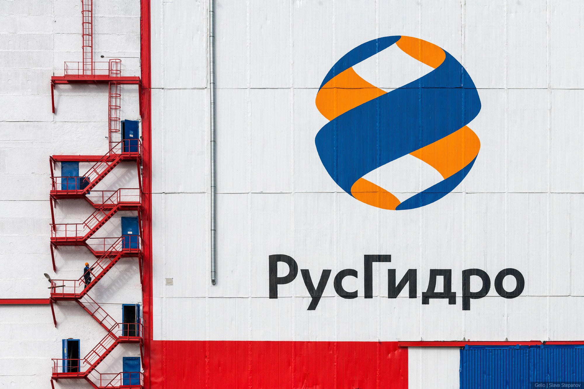 Индустриальный минимализм: логотип компании «РусГидро» на белом фасаде здания рядом с яркой красной лестницей, фото Slava Stepanov.