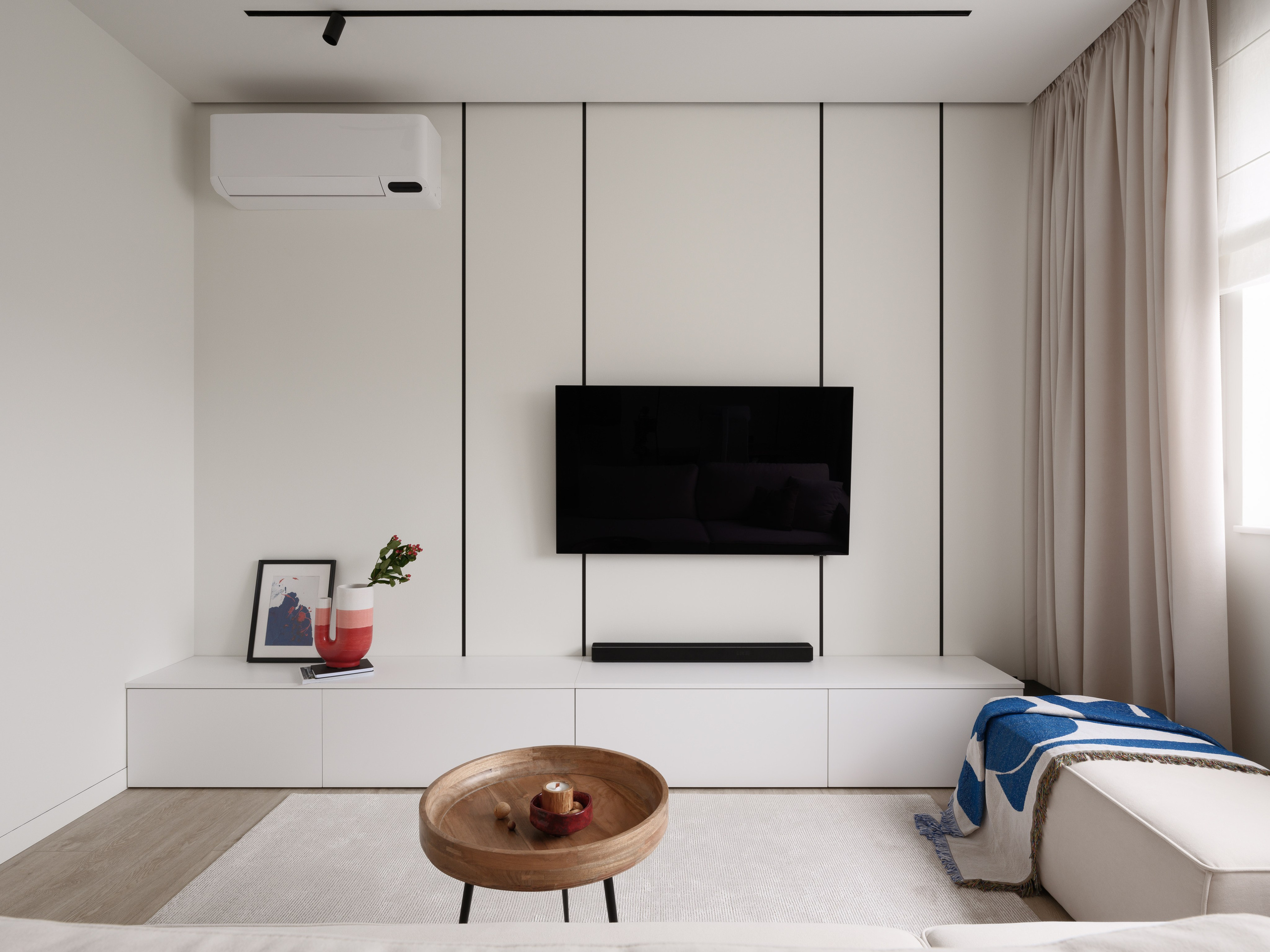 Современная гостиная в стиле минимализм: телевизор на стене, белая тумба и бежевые шторы. Интерьер создан дизайнерами Евгенией Княжевой и Владленой Приваловой. Фотограф — Сергей Денисенко