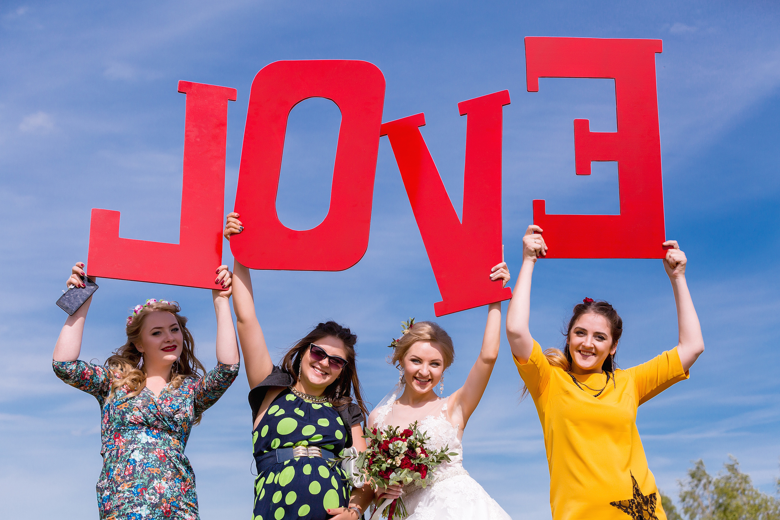 невеста с подружками на фоне неба с красными буквами