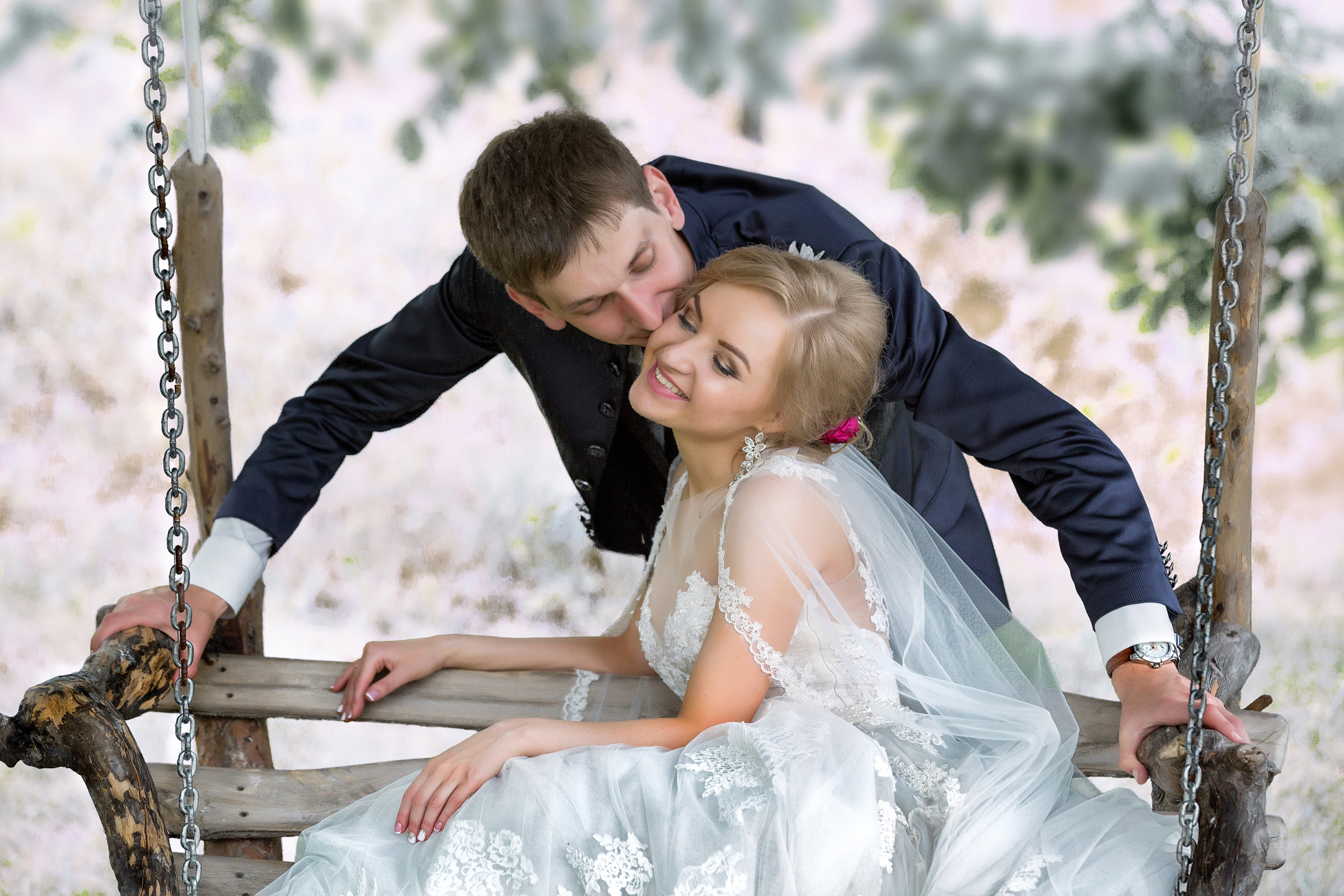 невеста сидит на качелях, жених сзади целует ее