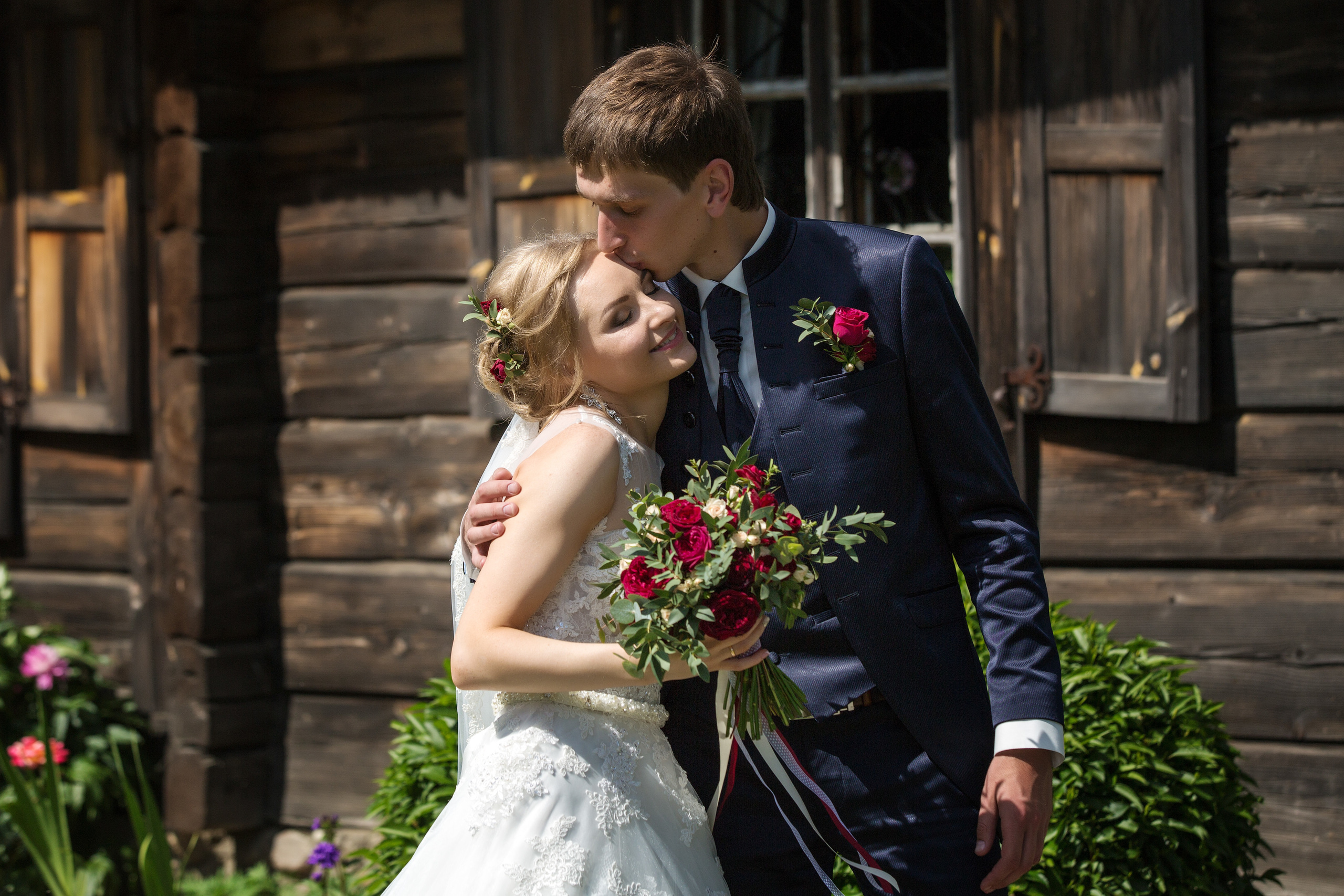 жених с невестой обнимаются на фоне старого деревянного домика