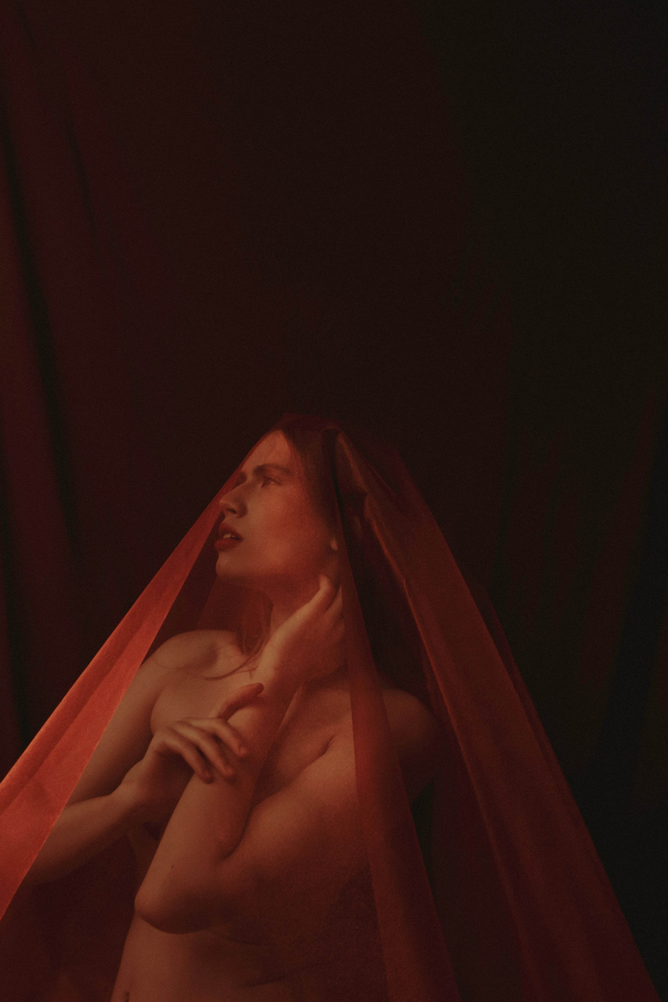 На бордовом фоне девушка покрытая красной тканью