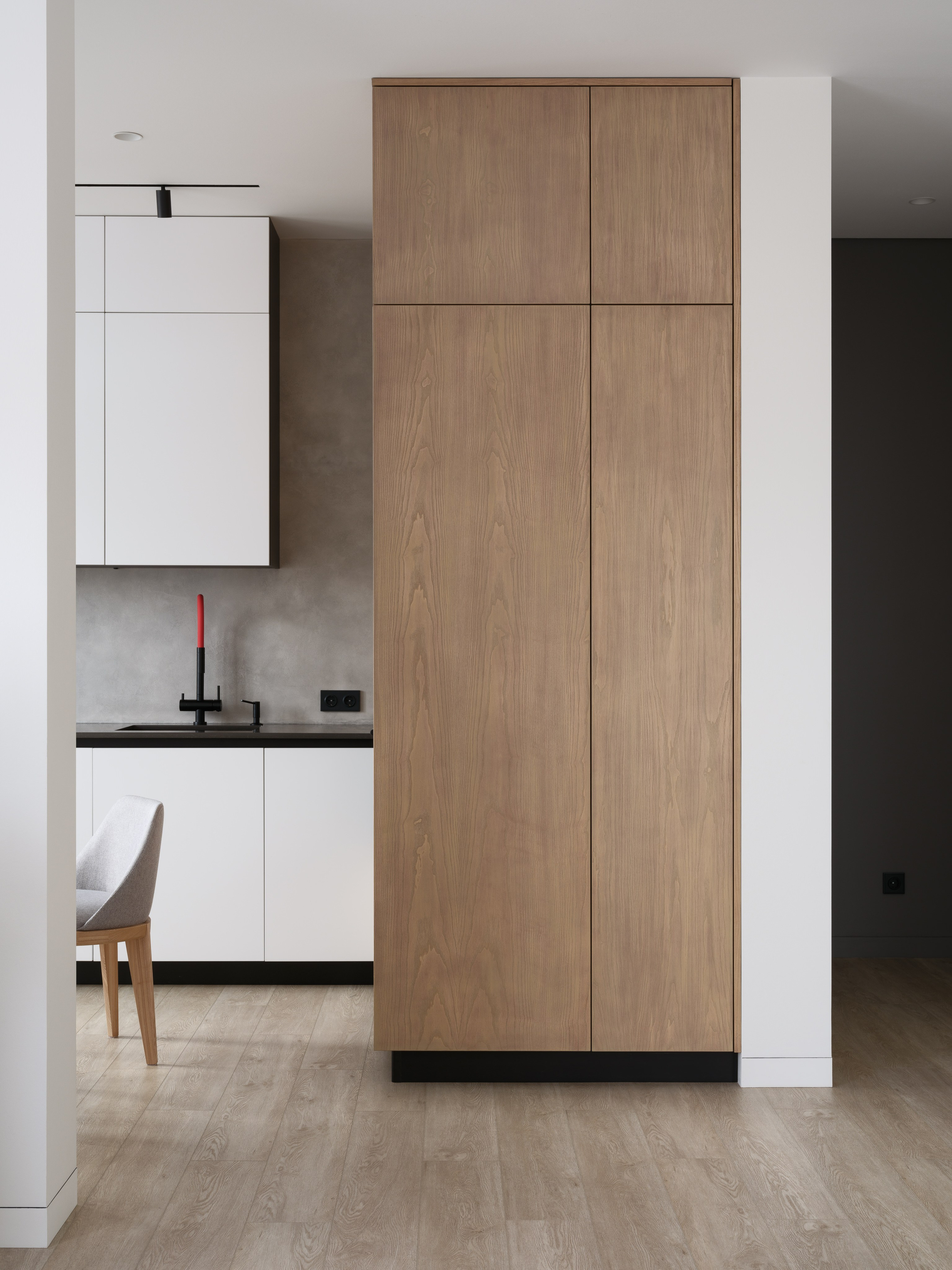 Современная кухня с высоким деревянным шкафом, белыми фасадами без ручек и черным смесителем с красным акцентом. Дизайн Евгении Княжевой и Владлены Приваловой, фото Сергея Денисенко