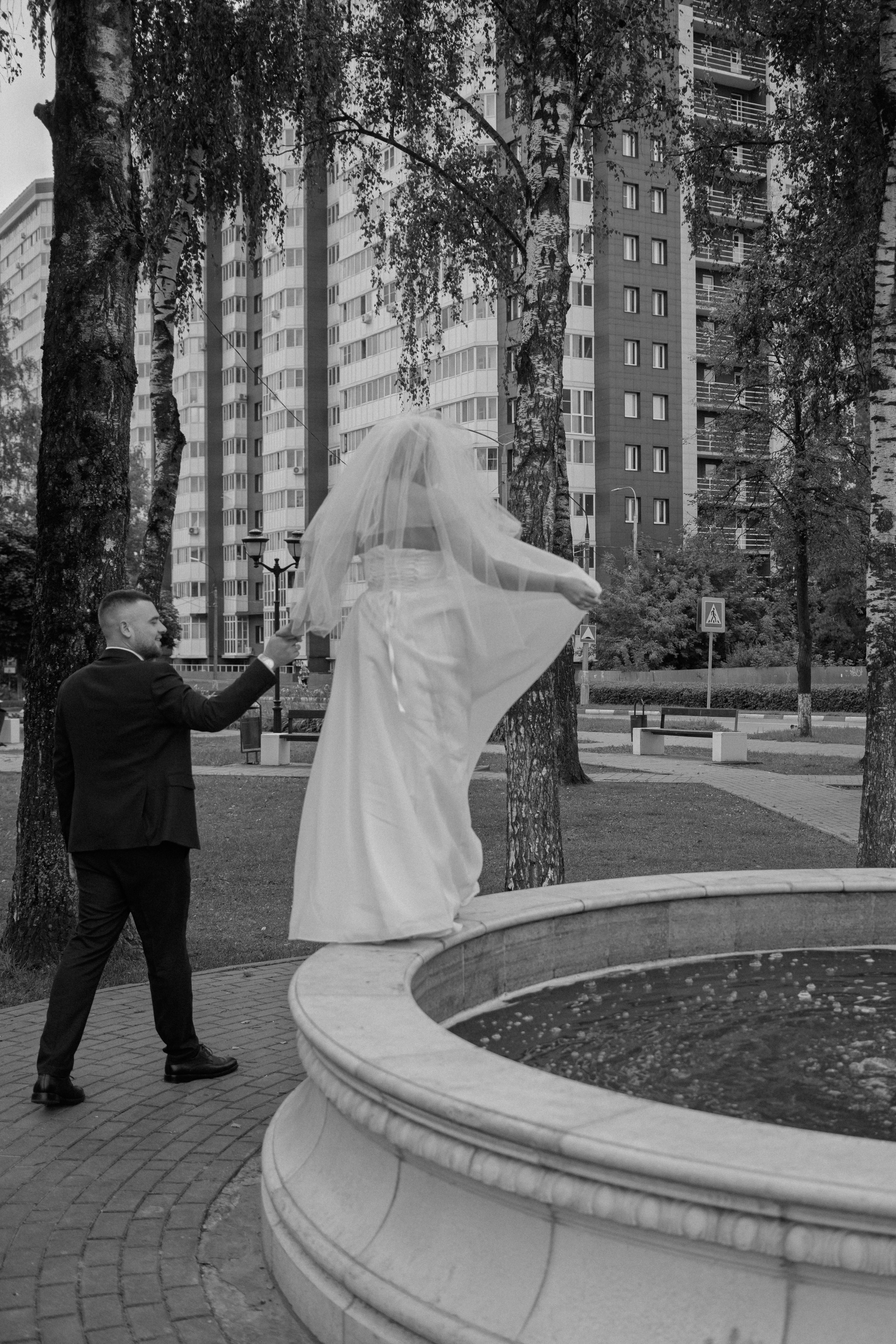 Живой кадр: невеста гуляет по фонтану в Старой Купавне, муж поддерживает её за руку.