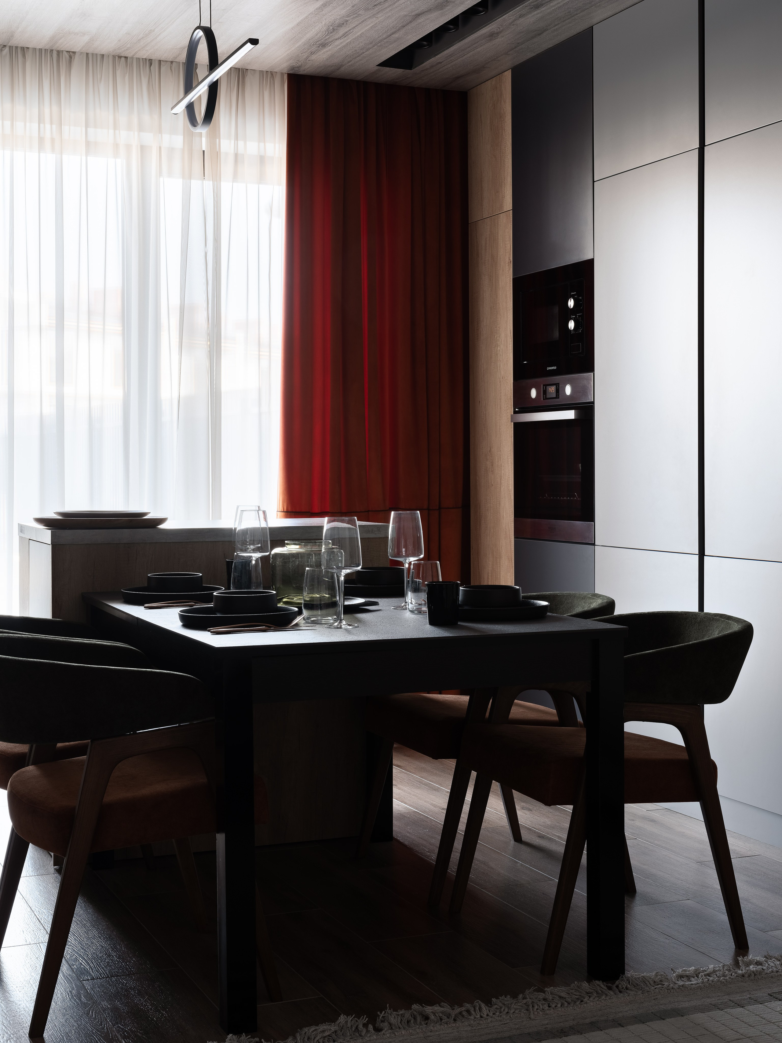 Интерьер столовой с современным черным столом, сервировкой, мягкими стульями и красными шторами на фоне кухни; проект дизайнера Екатерины Мищенко, фотография Сергея Денисенко.