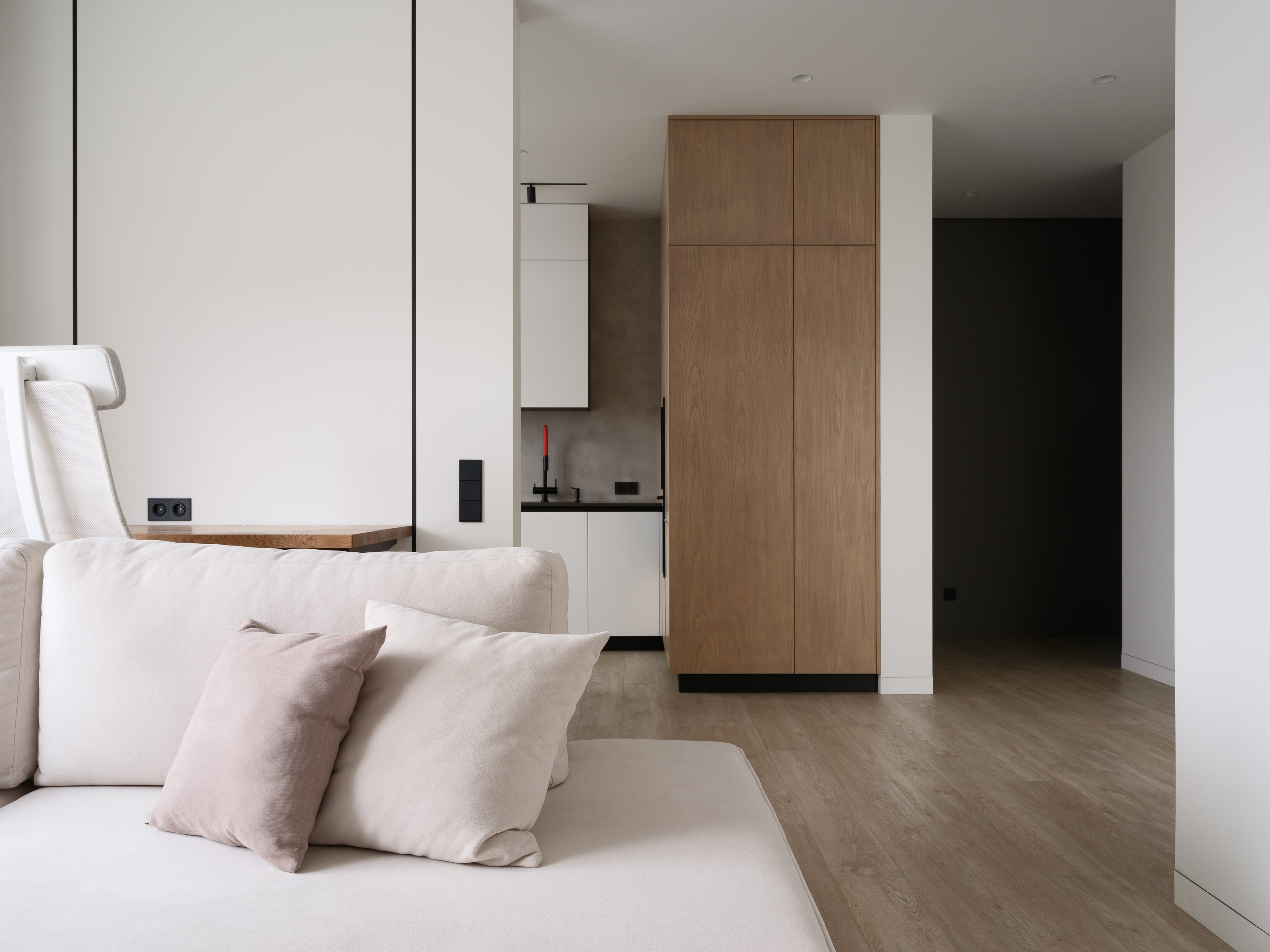 Современная квартира с открытой планировкой: уютная гостиная с бежевым диваном и кухней с высоким деревянным шкафом и белыми фасадами. Дизайн Евгении Княжевой и Владлены Приваловой, фото Сергея Денисенко