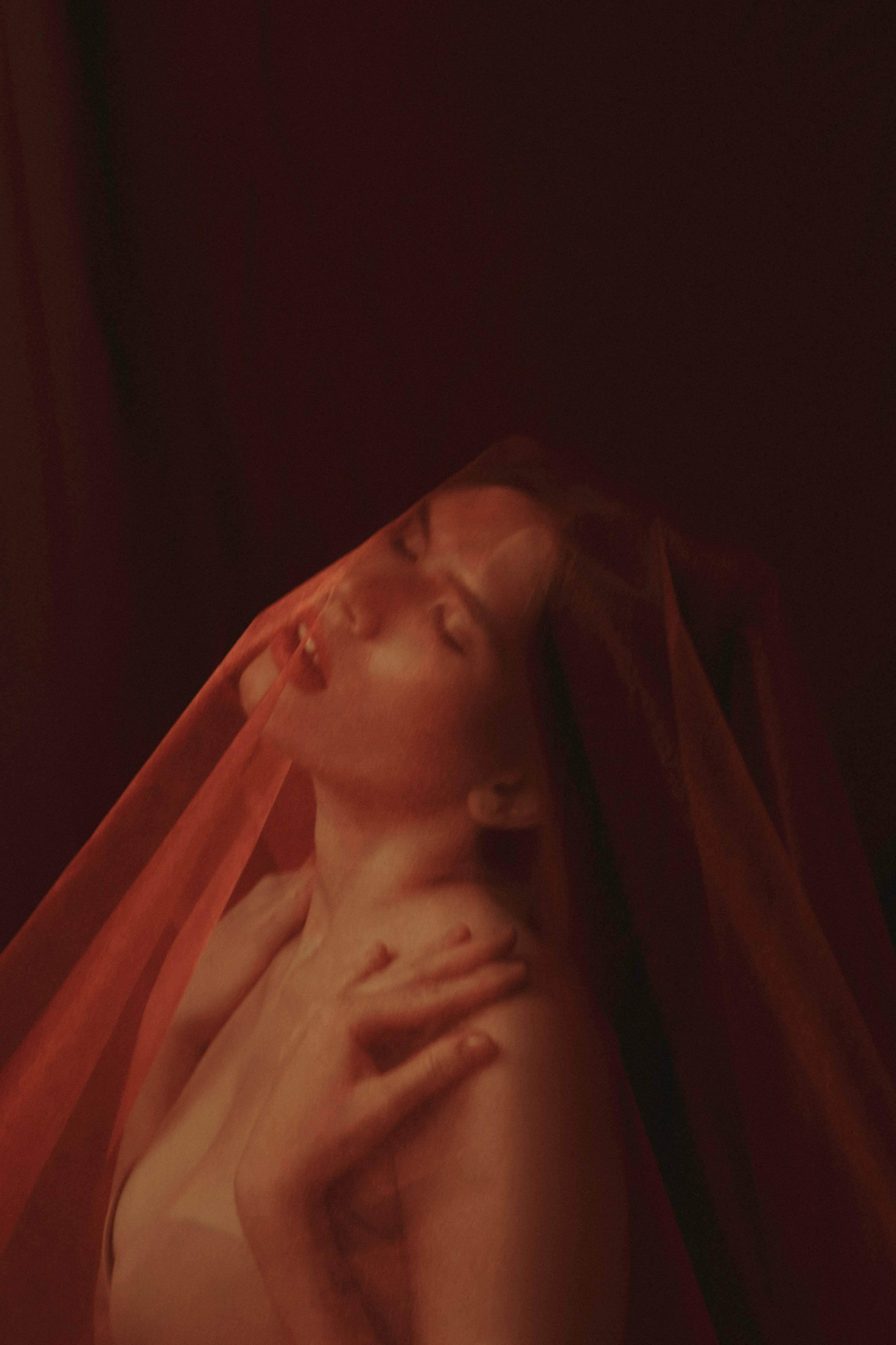 девушка покрытая красной тканью на бордовом фоне показывает эмоцию страсти 