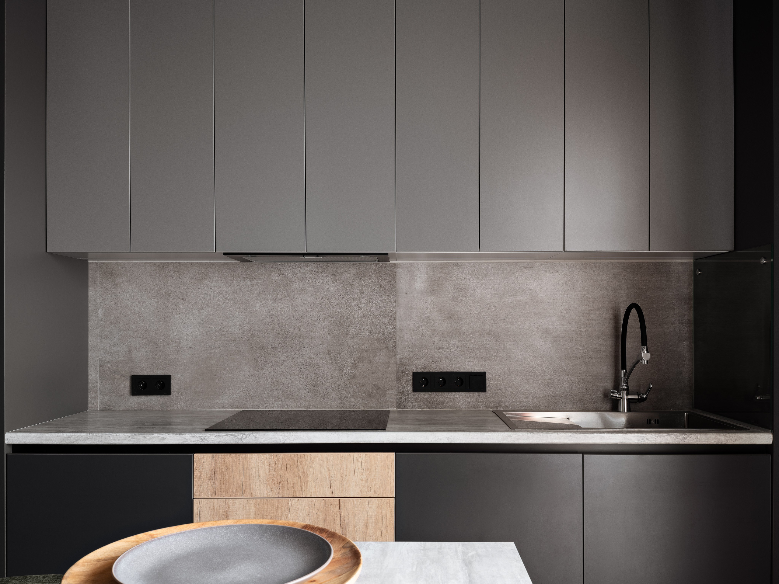Современная кухня в минималистичном стиле с серыми матовыми фасадами, бетонным фартуком и черной техникой; проект дизайнера Екатерины Мищенко, интерьерная фотография Сергея Денисенко.