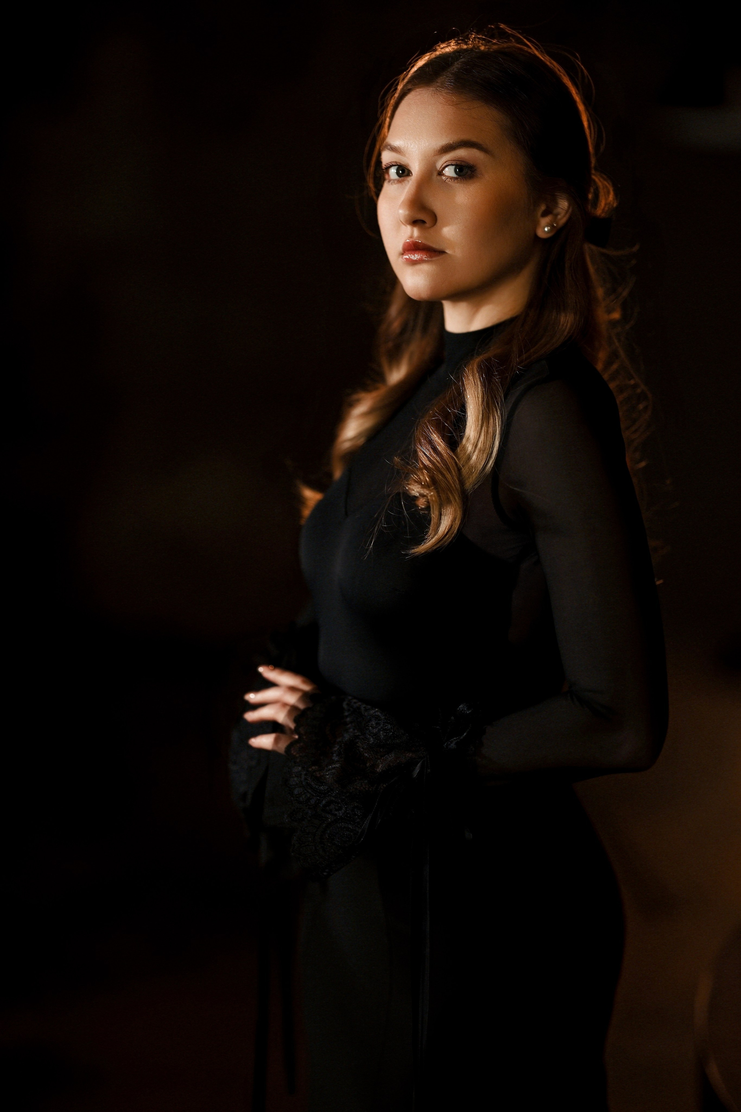 Студийный портрет девушки в черном платье с прозрачными кружевными рукавами, темный фон, драматичное освещение, длинные волнистые волосы