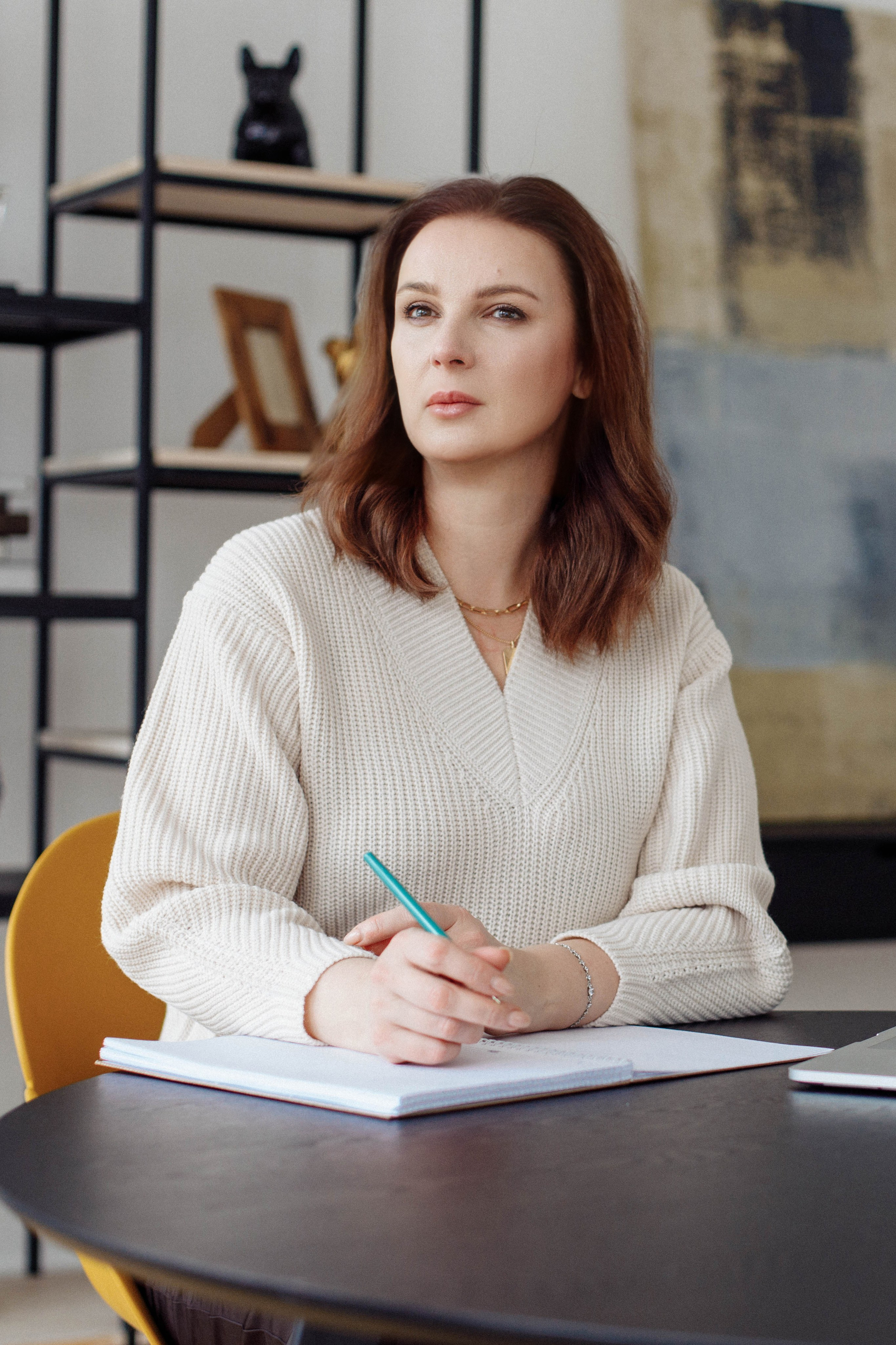 Естественный рабочий момент: психолог делает записи за столом, отвлекаясь на размышления у окна.