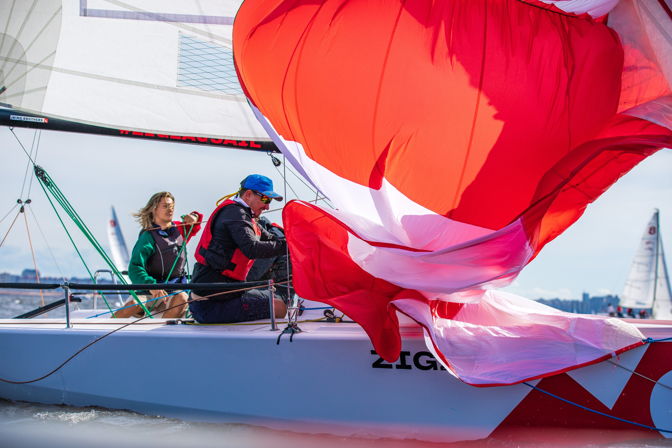 Красно-белый генакер развевается во время постановки. Спортсмены на яхте класса MX700.