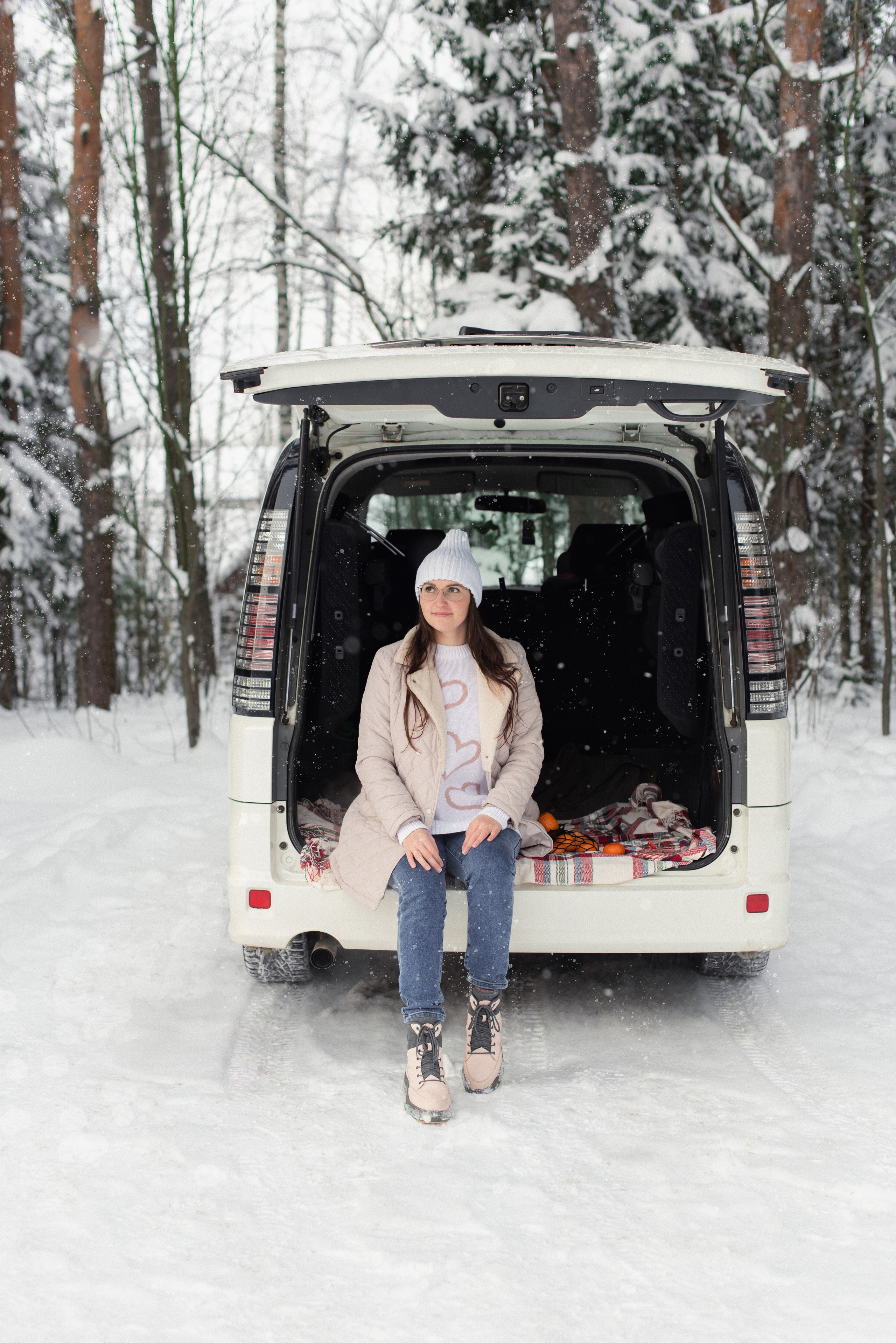 Зимний пейзаж: девушка, цитрусовые, белый автомобиль с открытым багажником — съёмка в лесной зоне.