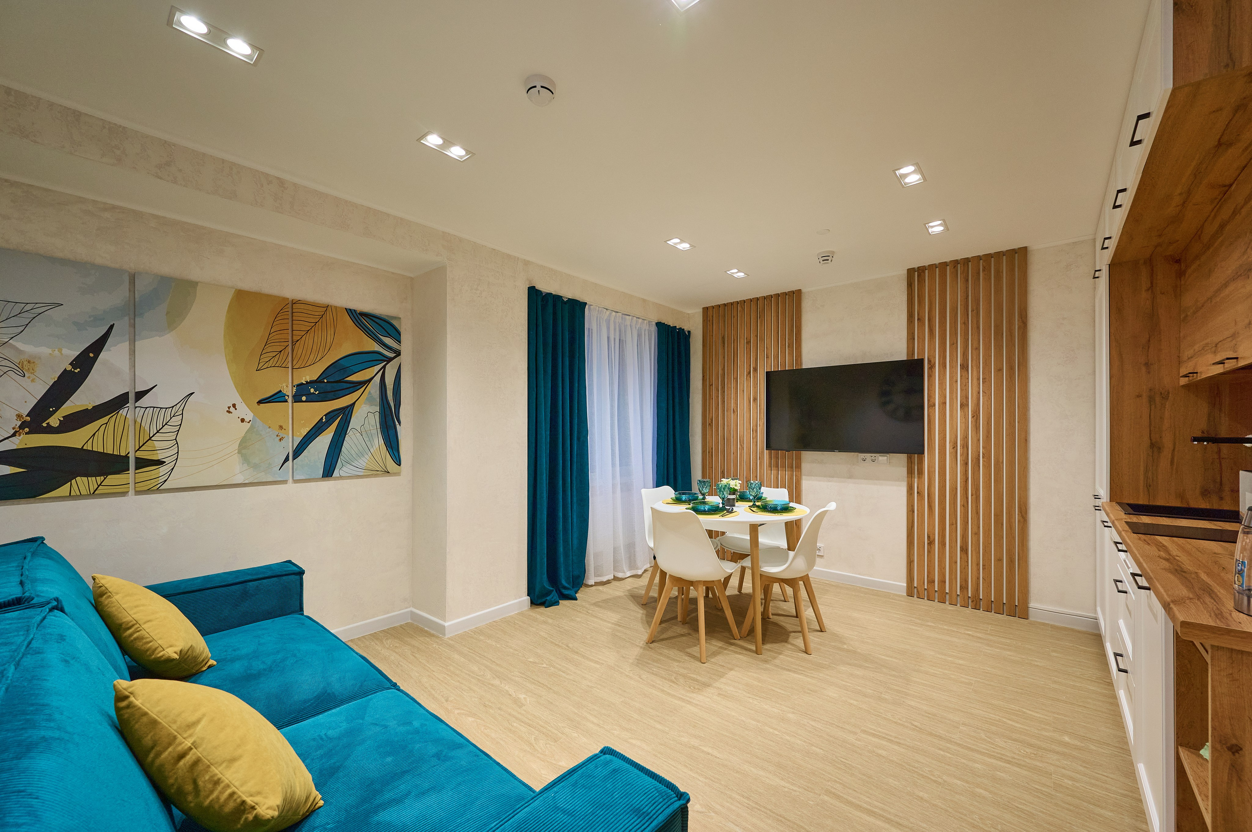 кухня синий диван синие шторы круглый белый стол стулья белые полки и ящики телевизор деревянный стол раковина