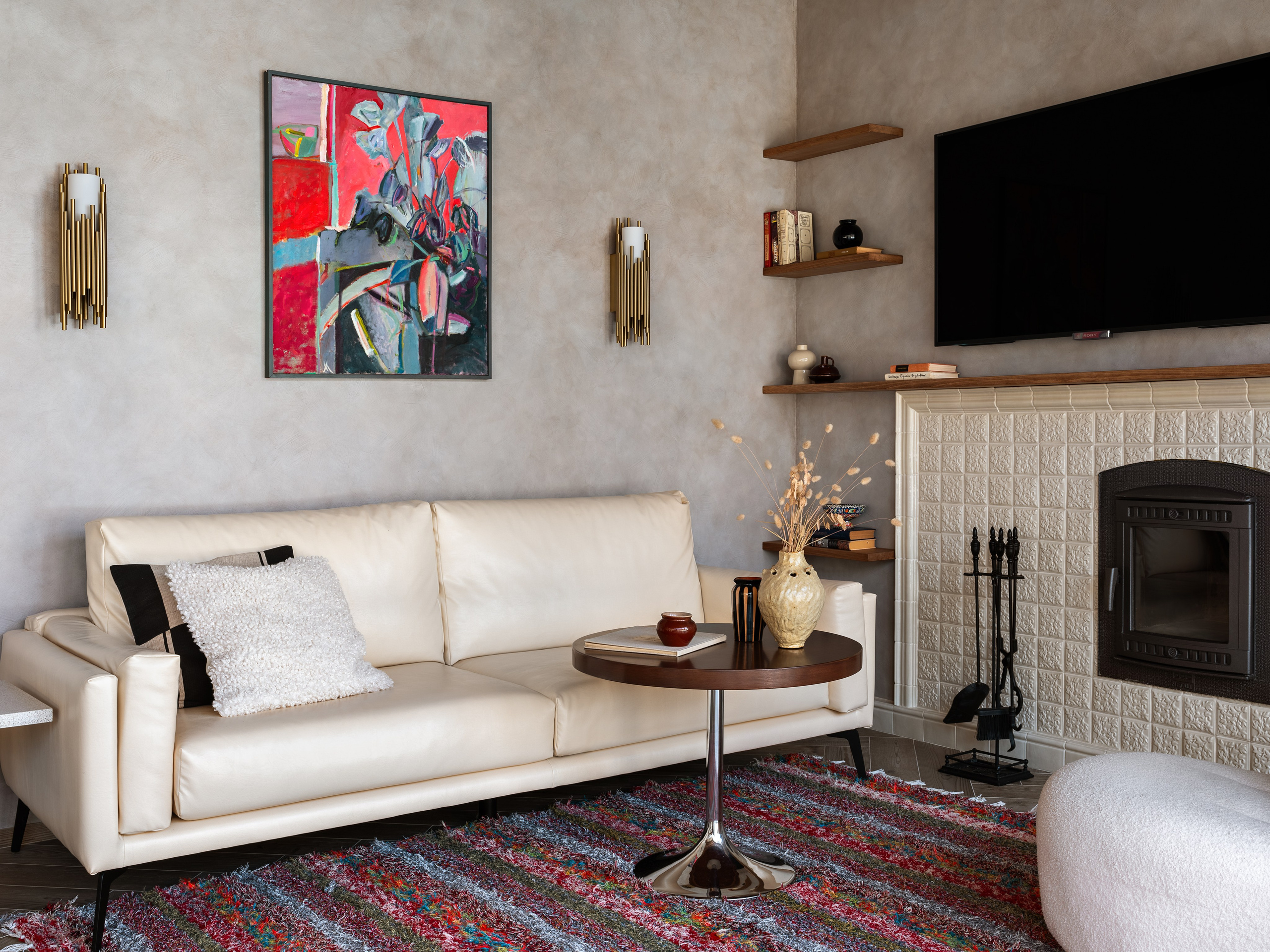 Интерьер гостиной с белым диваном, цветным ковром ручной работы, абстрактной картиной и камином в отделке плиткой; стильный дизайн Наталии Шелепниковой, стилист София Калбазова, фотограф Сергей Денисенко.
