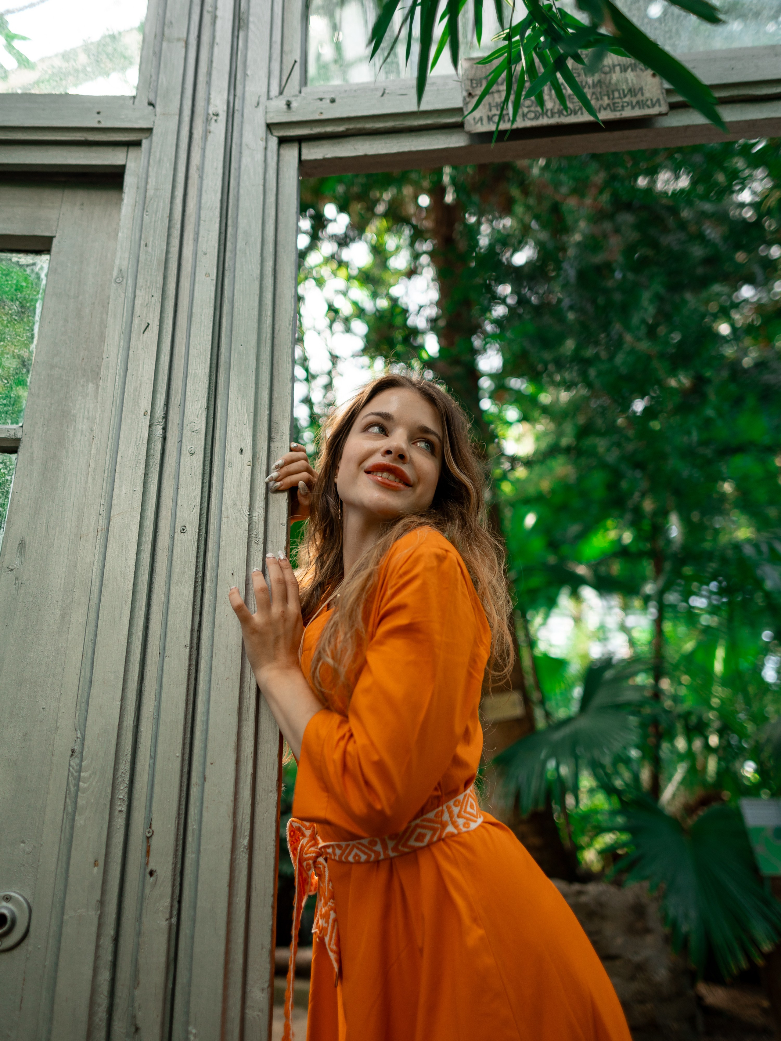 Девушка в оранжевом платье стоит на фоне зелени