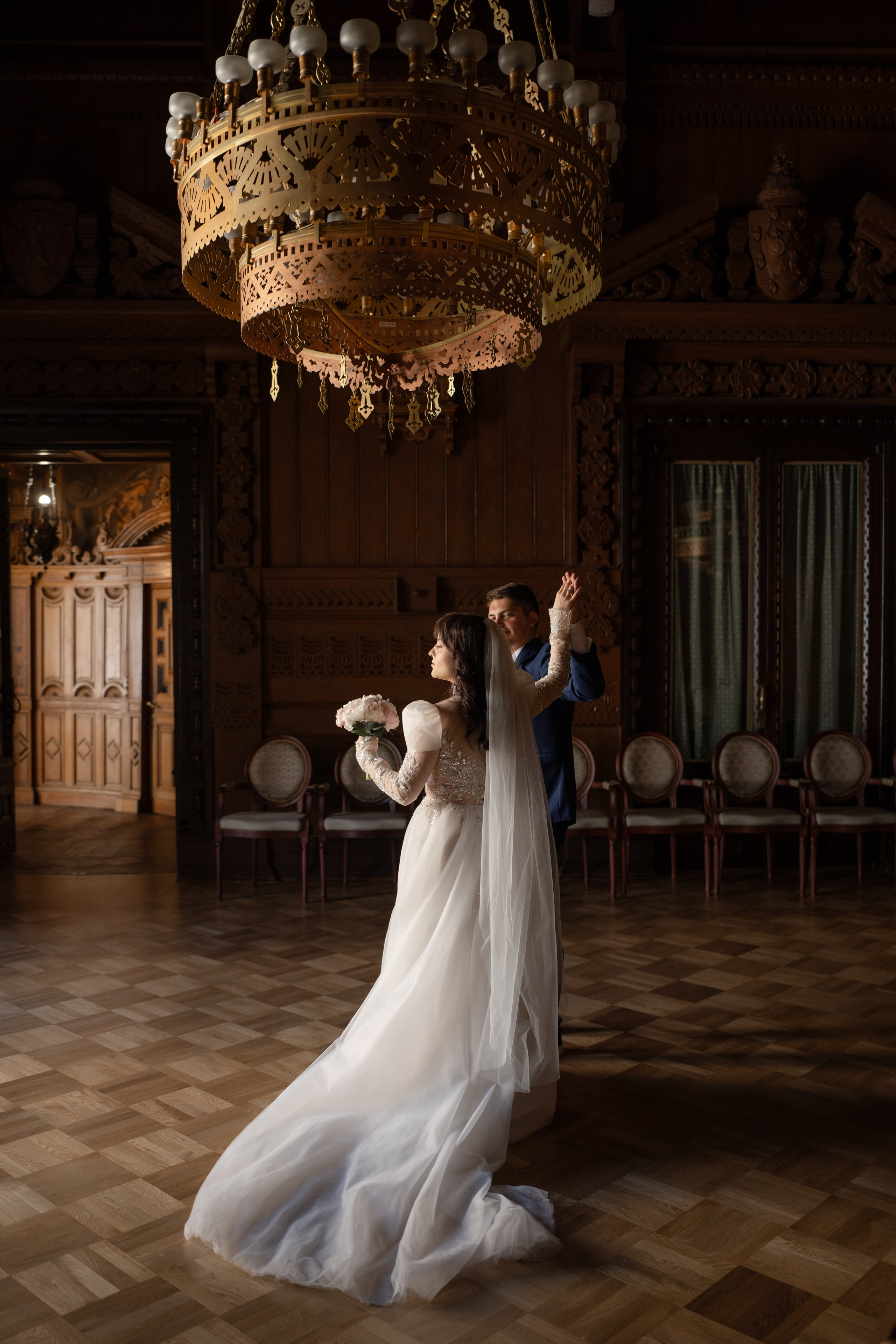 Свадебная фотосессия в Доме ученых, Дворце князя Владимира в Санкт-Петербурге. Жених с невестой в дубовом зале танцуют под огромными люстрами