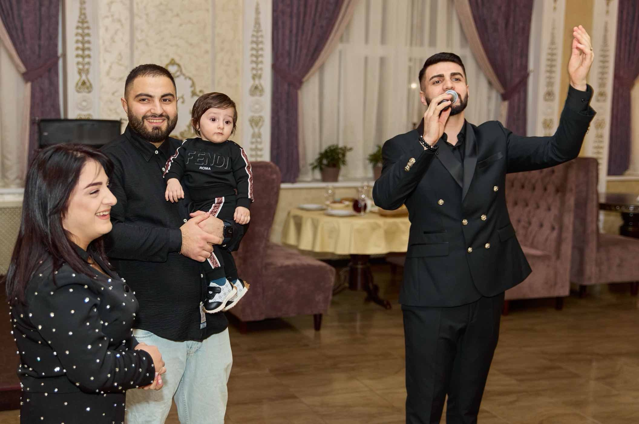 Ведущий с микрофоном рядом с родителями именинника