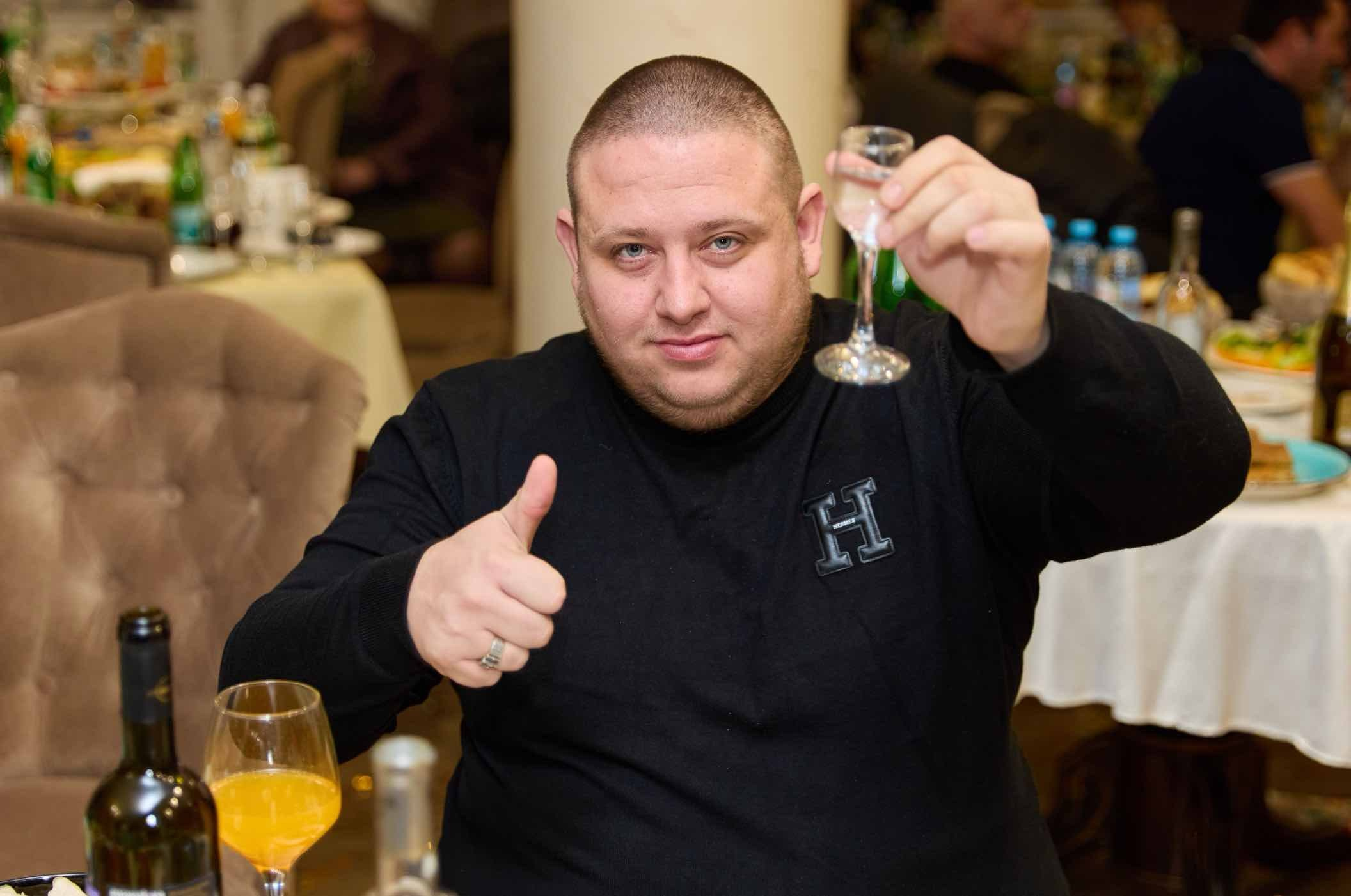 Гость поднял бокал и показывает большой палец за столом