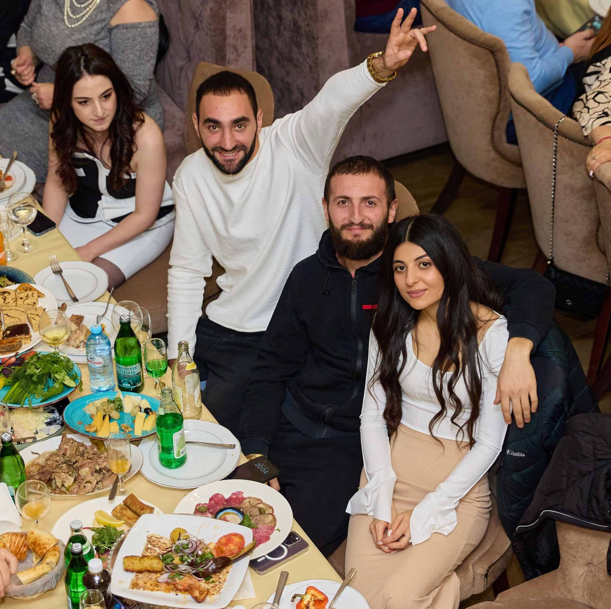 Гости за столом на годовасии, один поднял руку