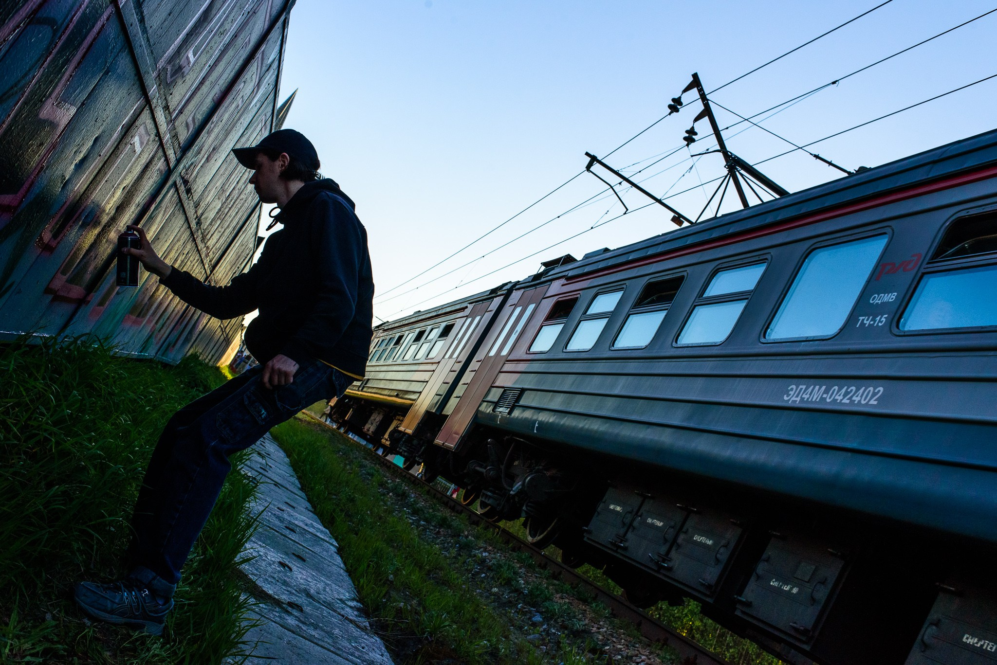 Граффити художник рисует на лайне вдоль железной дороги