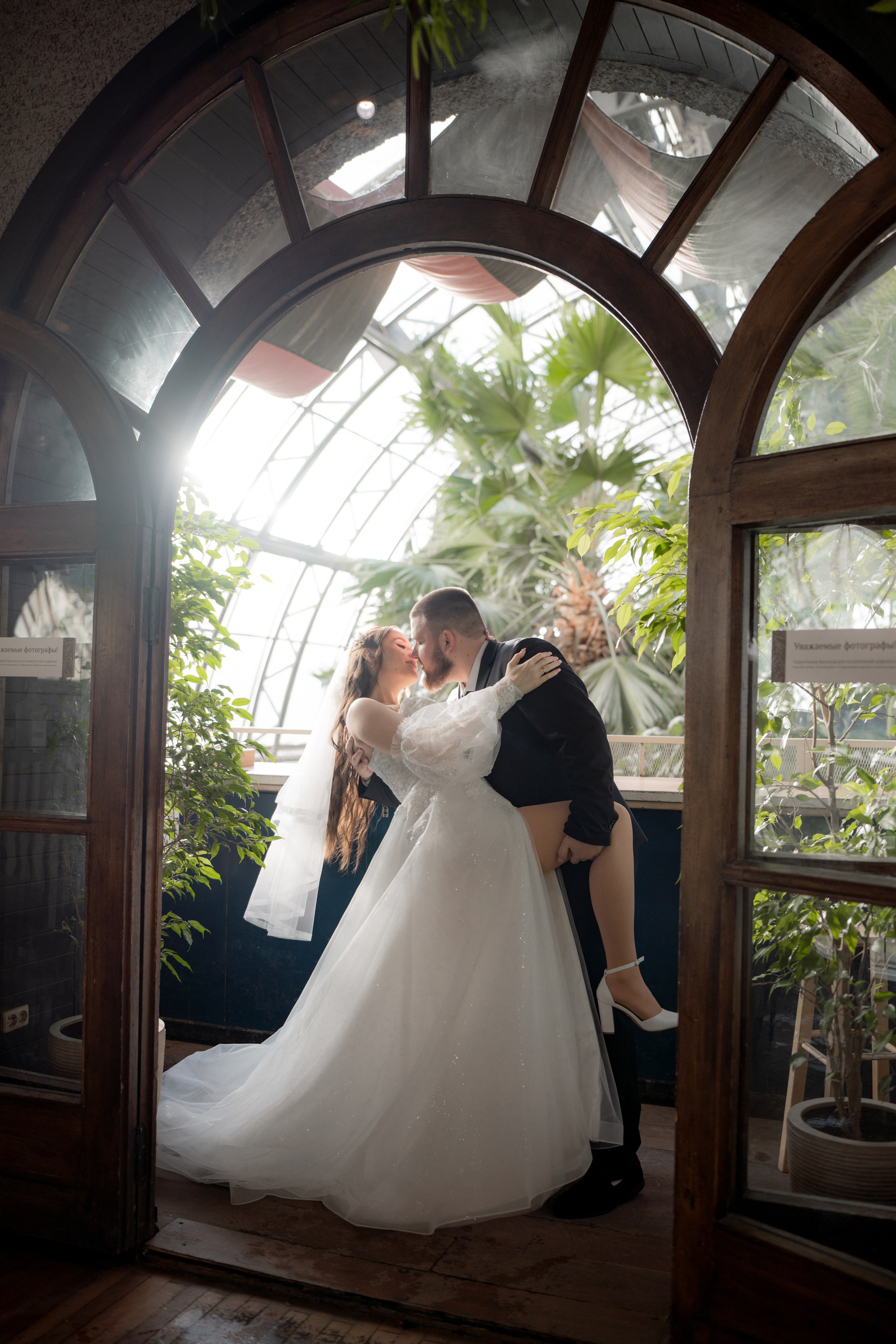 Свадебная фотография в Оранжерее Таврического сада Санкт-Петербурге. Жених и невеста обнимаются и  красиво целуются в лучах света