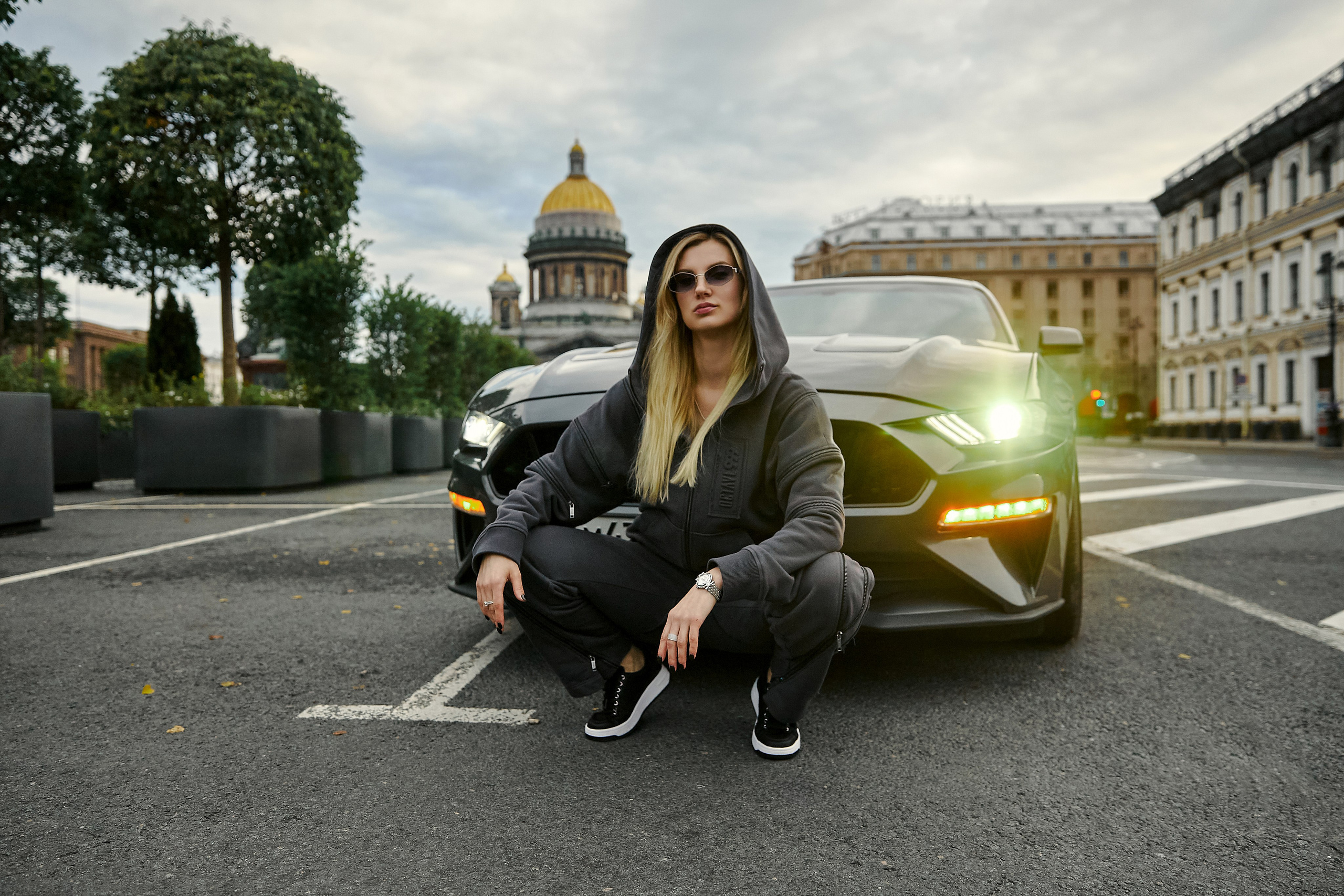девушка в спортивном костюме на фоне мустанга в центре Петербурга 