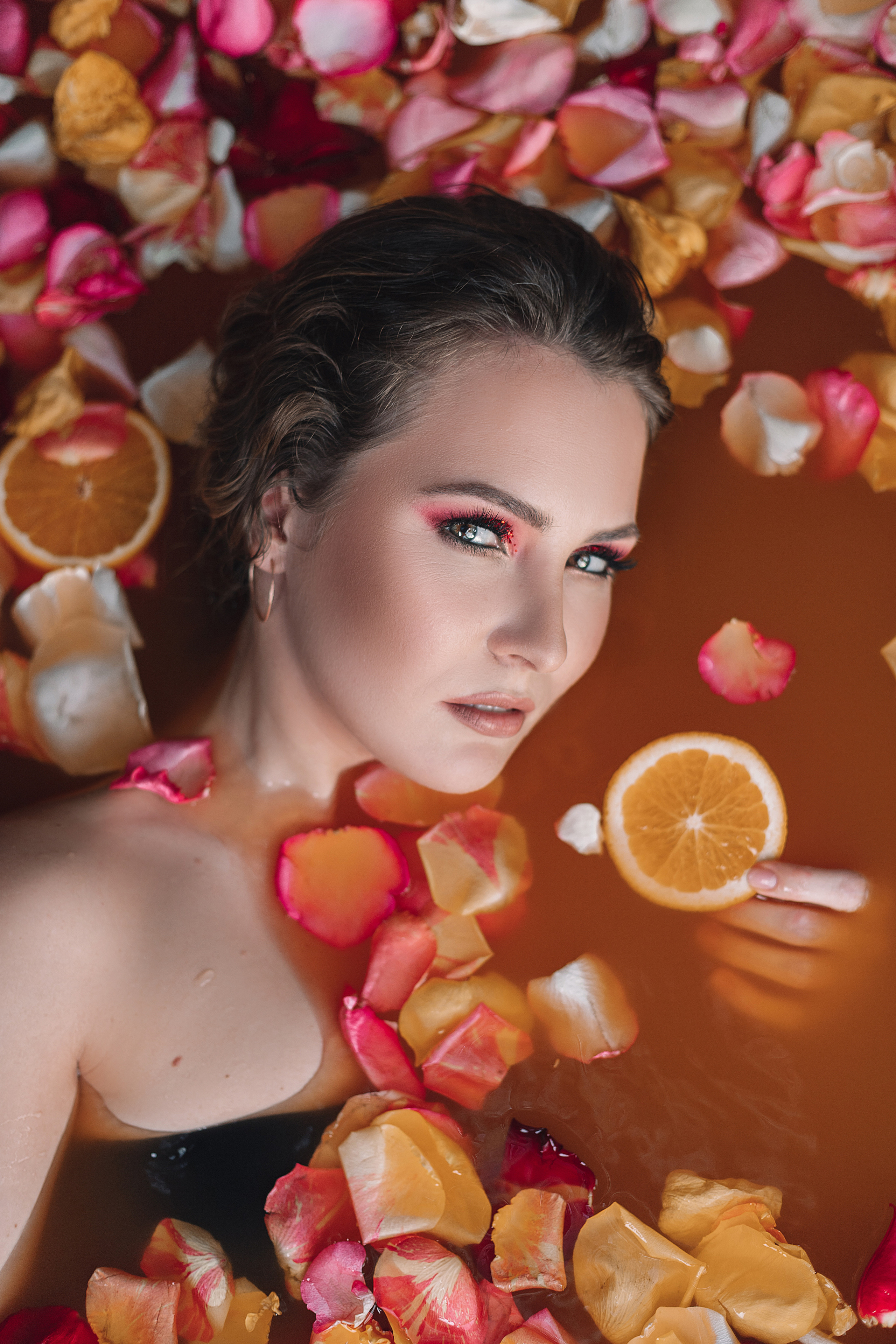 Девушка в ванной с лепестками цветов и апельсинами