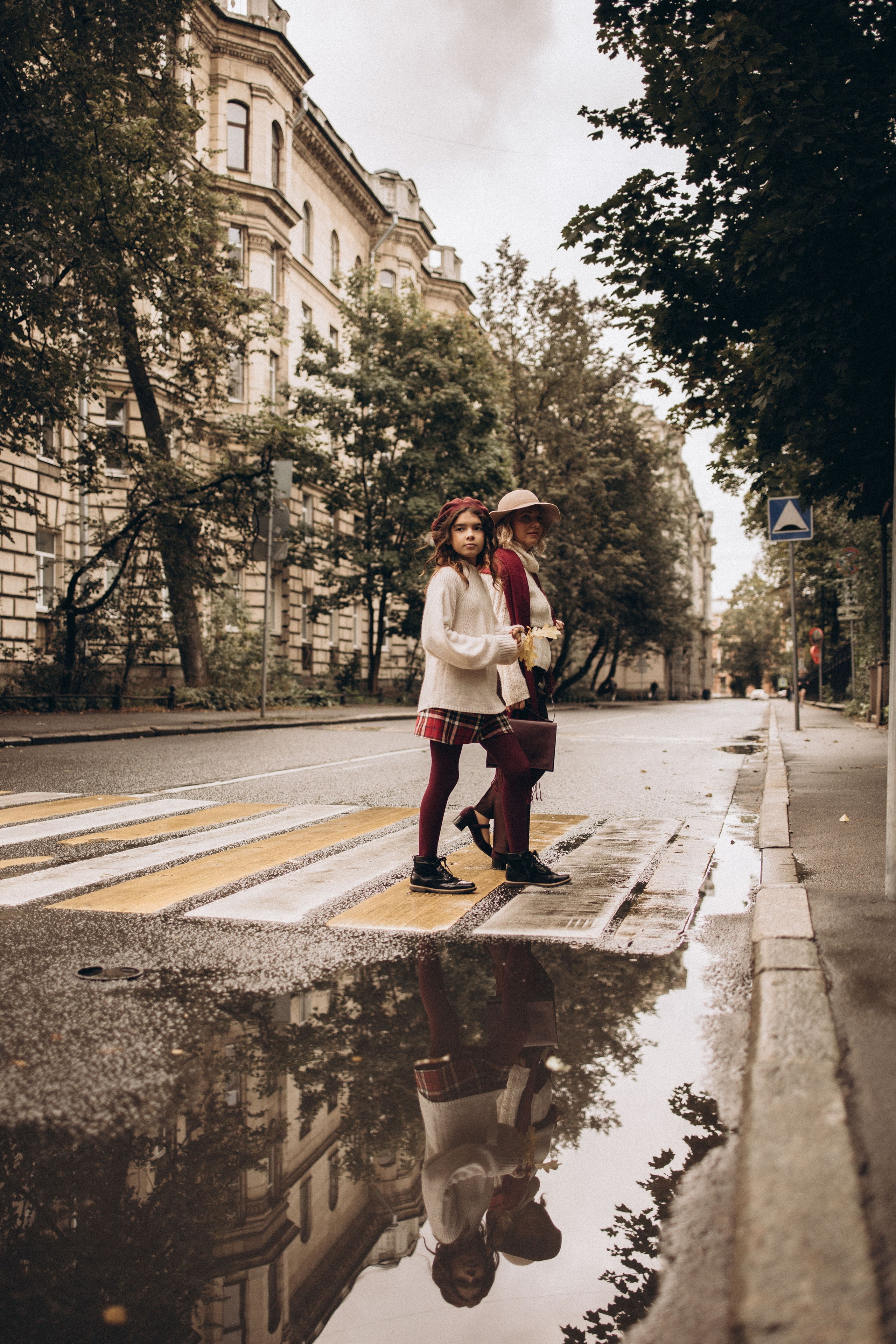 мама и дочка идут по пешеходному переходу и в лужах видно их отражение