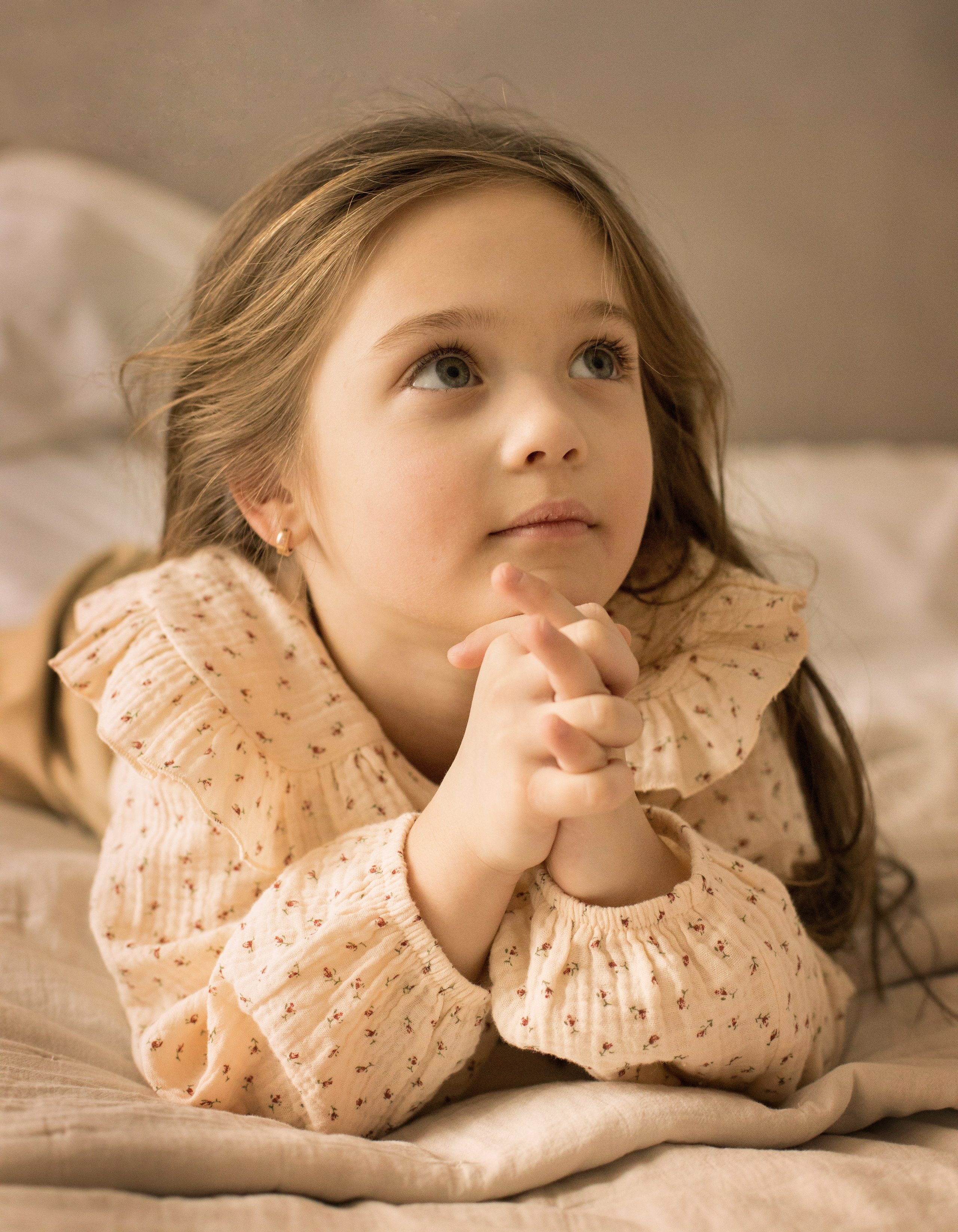 Портрет девочки с русыми волосами в бежевой кофточке лежа на кровати