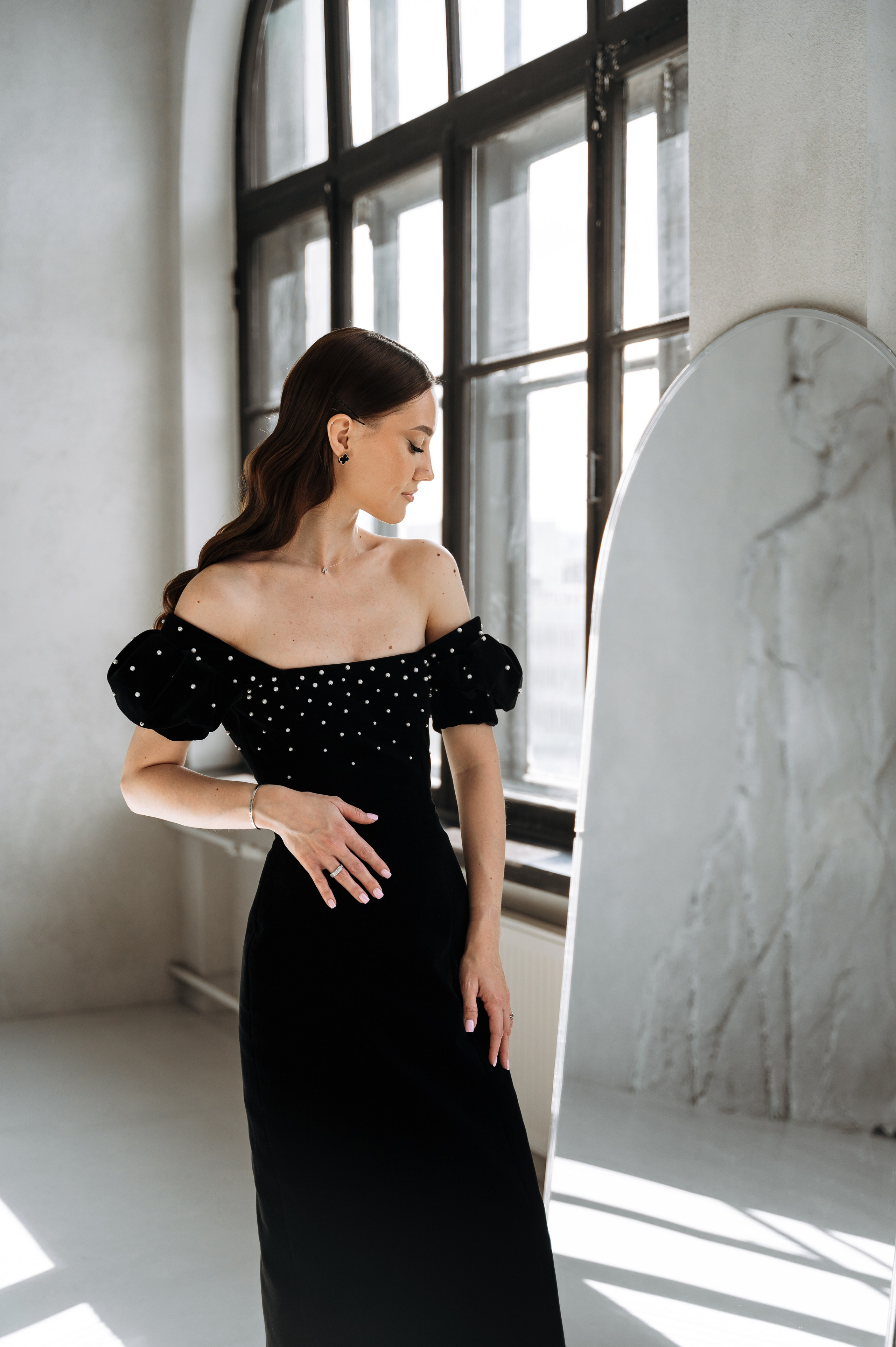 девушка в вечернем бархатном платье стоит напротив зеркала