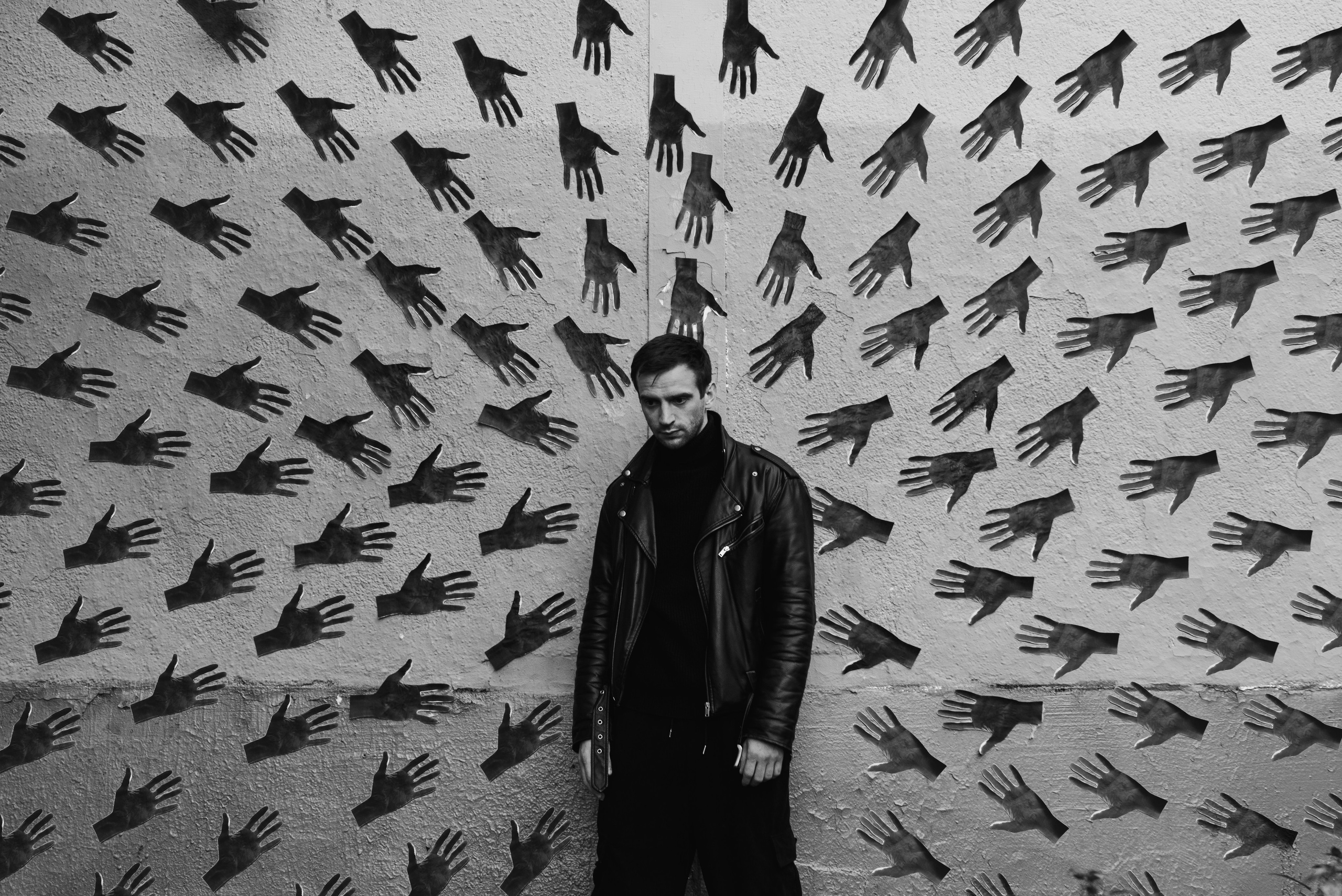 Актёр Николай Омельяненко позирует на фоне стены, где изображено много рук