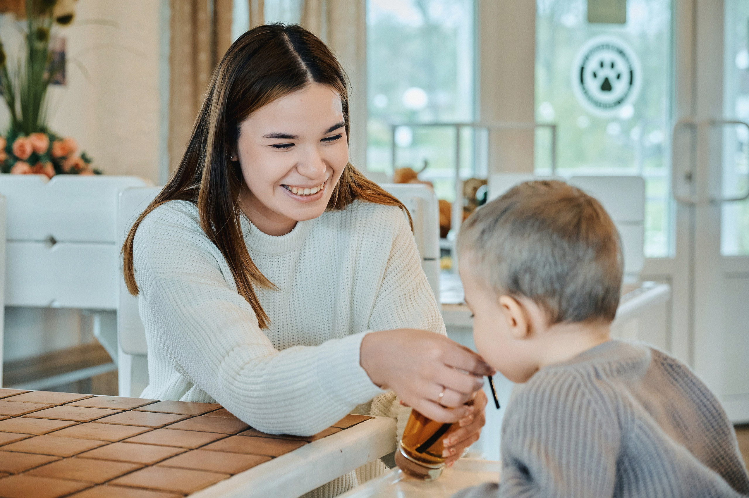 Женщина с улыбкой помогает мальчику пить через соломинку из стакана