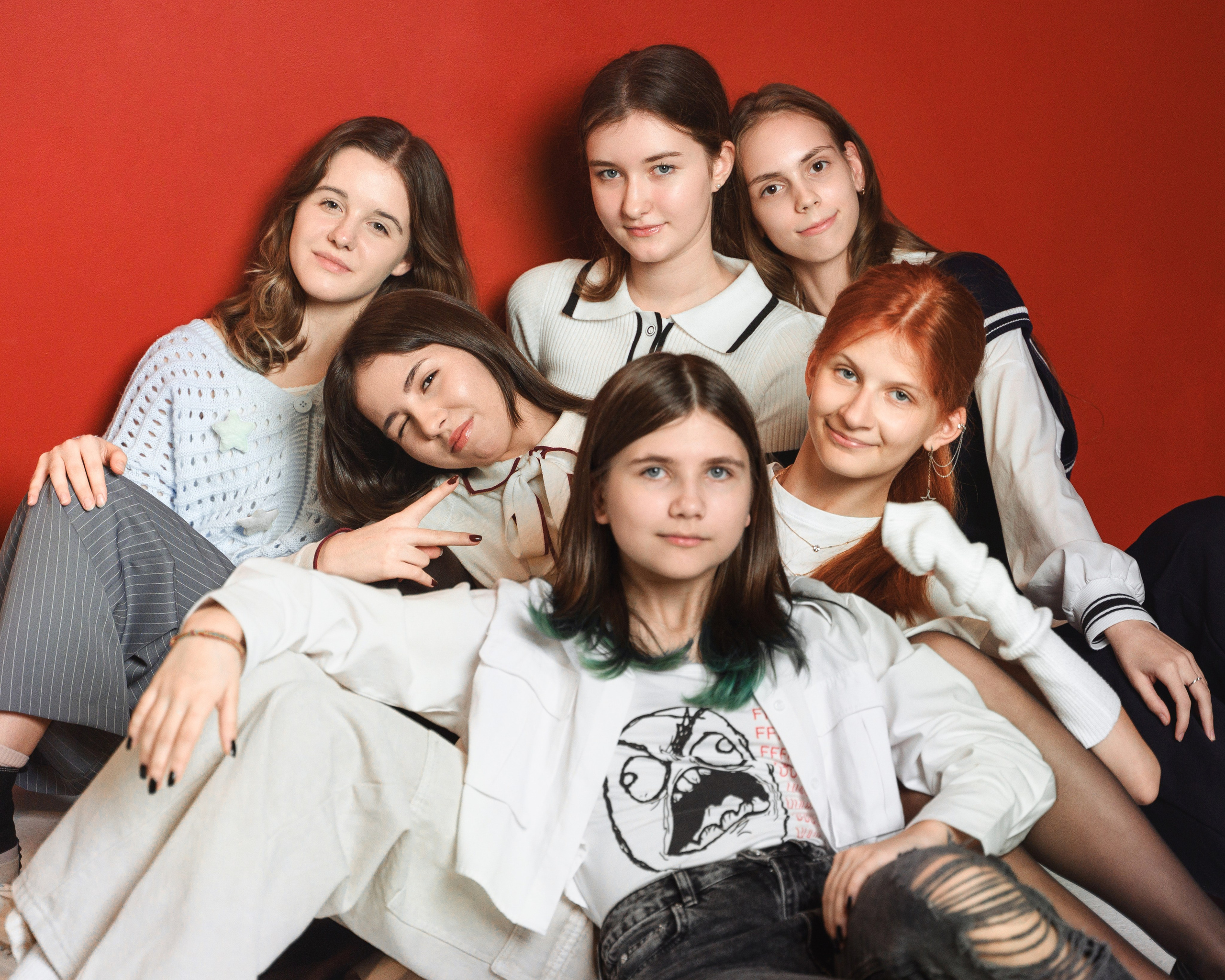 Группа девушек позирует в плотной композиции на ярком красном фоне.