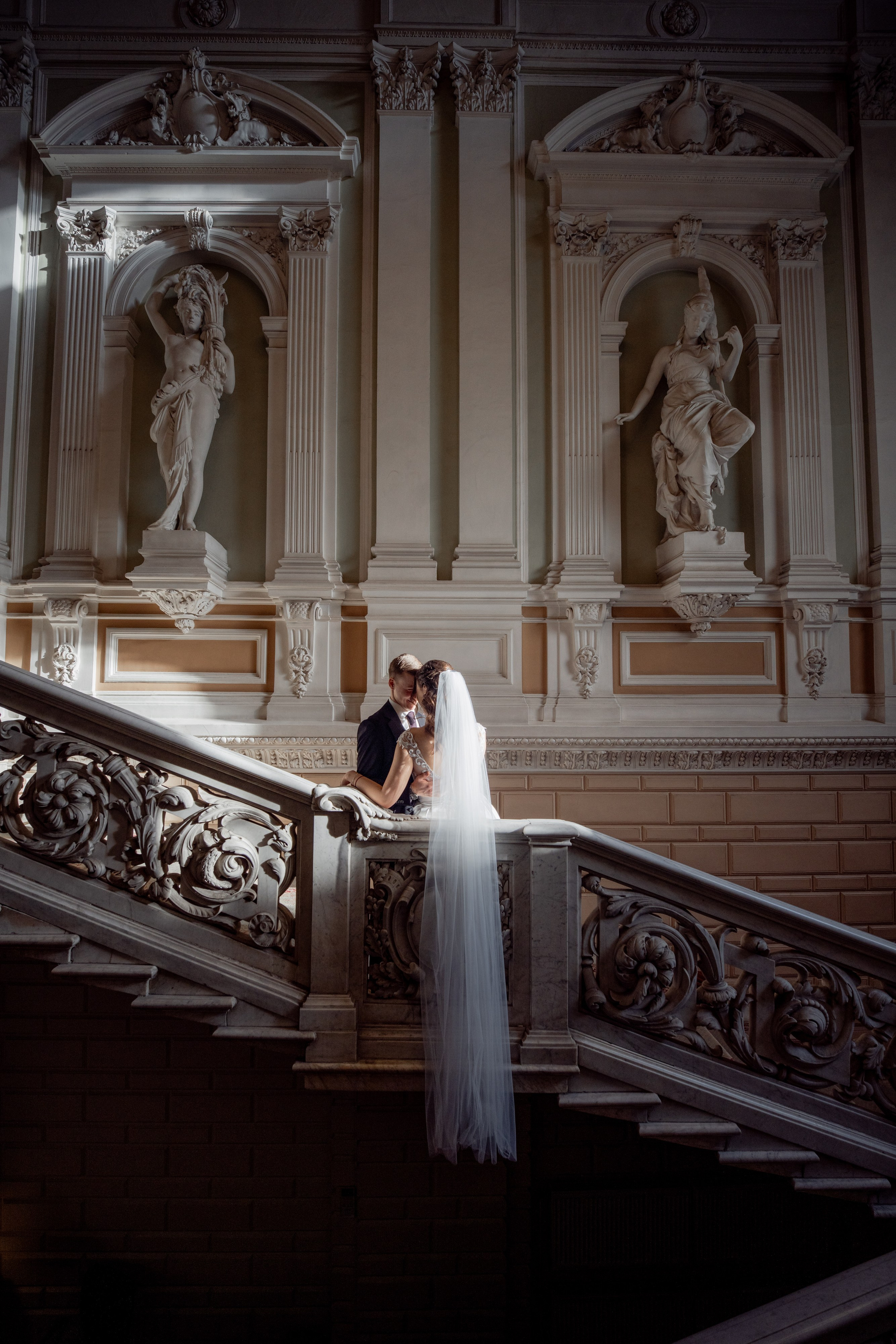Свадебная фотосессия в Санкт-Петербурге во дворце  бракосочетания №1 на Английской набережной. Невеста и жених стоят на освещенной солнцем лестнице лицом к друг другу и фата свисает вниз
