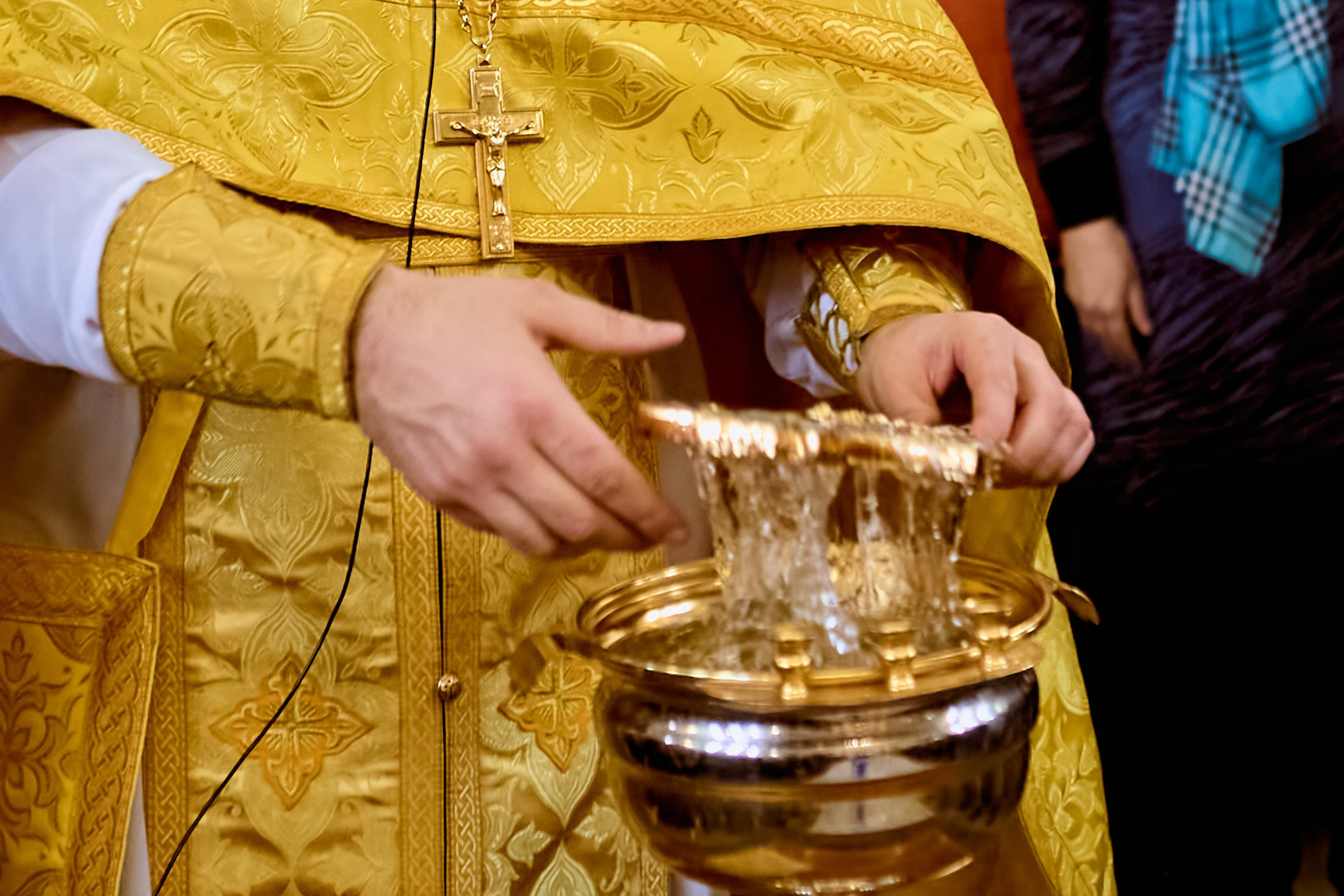 Руки священника с крестом из чаши со святой водой  с креста стекает вода