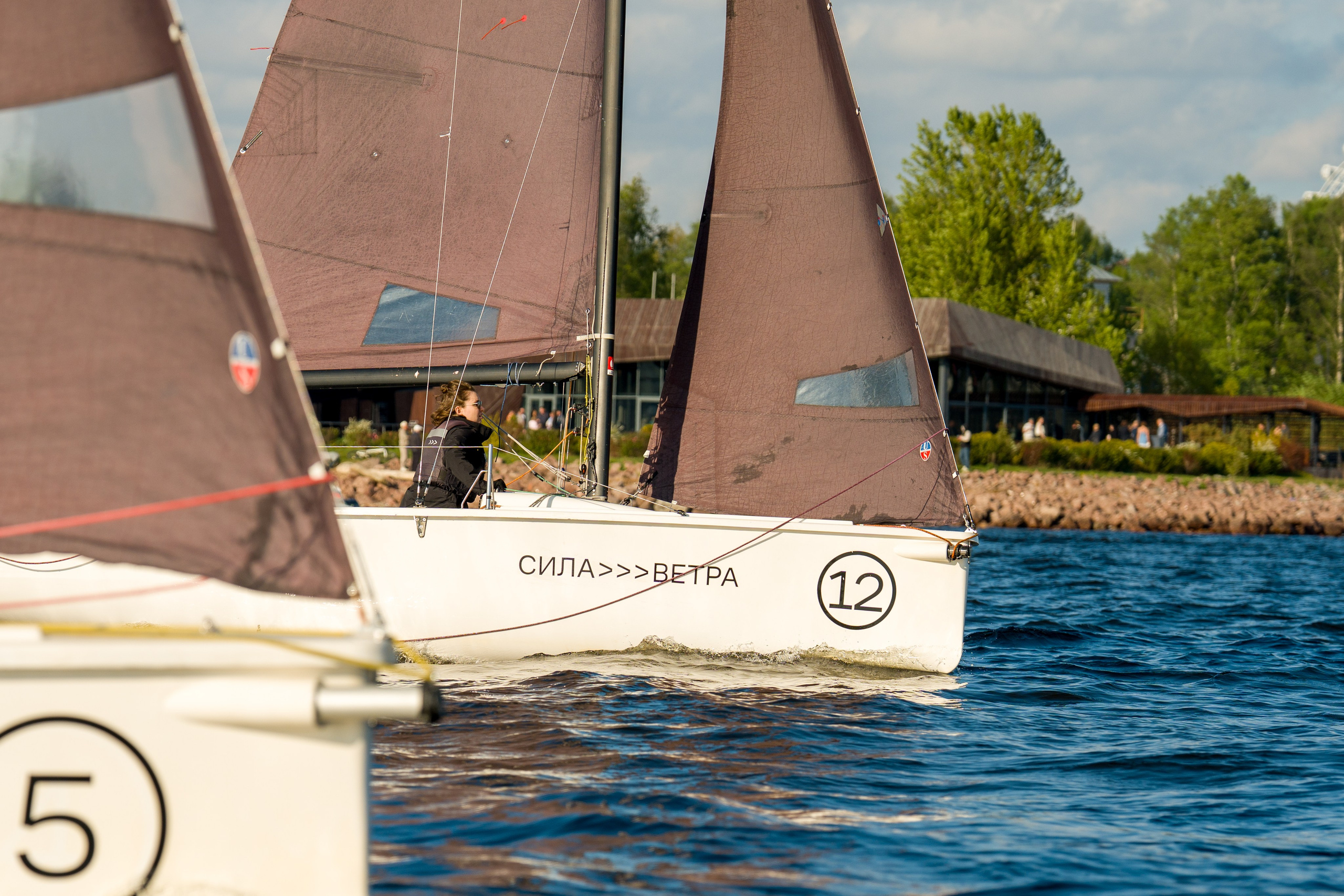 Sila Vetra SV20 charges downwind, shoreline buildings in the background
