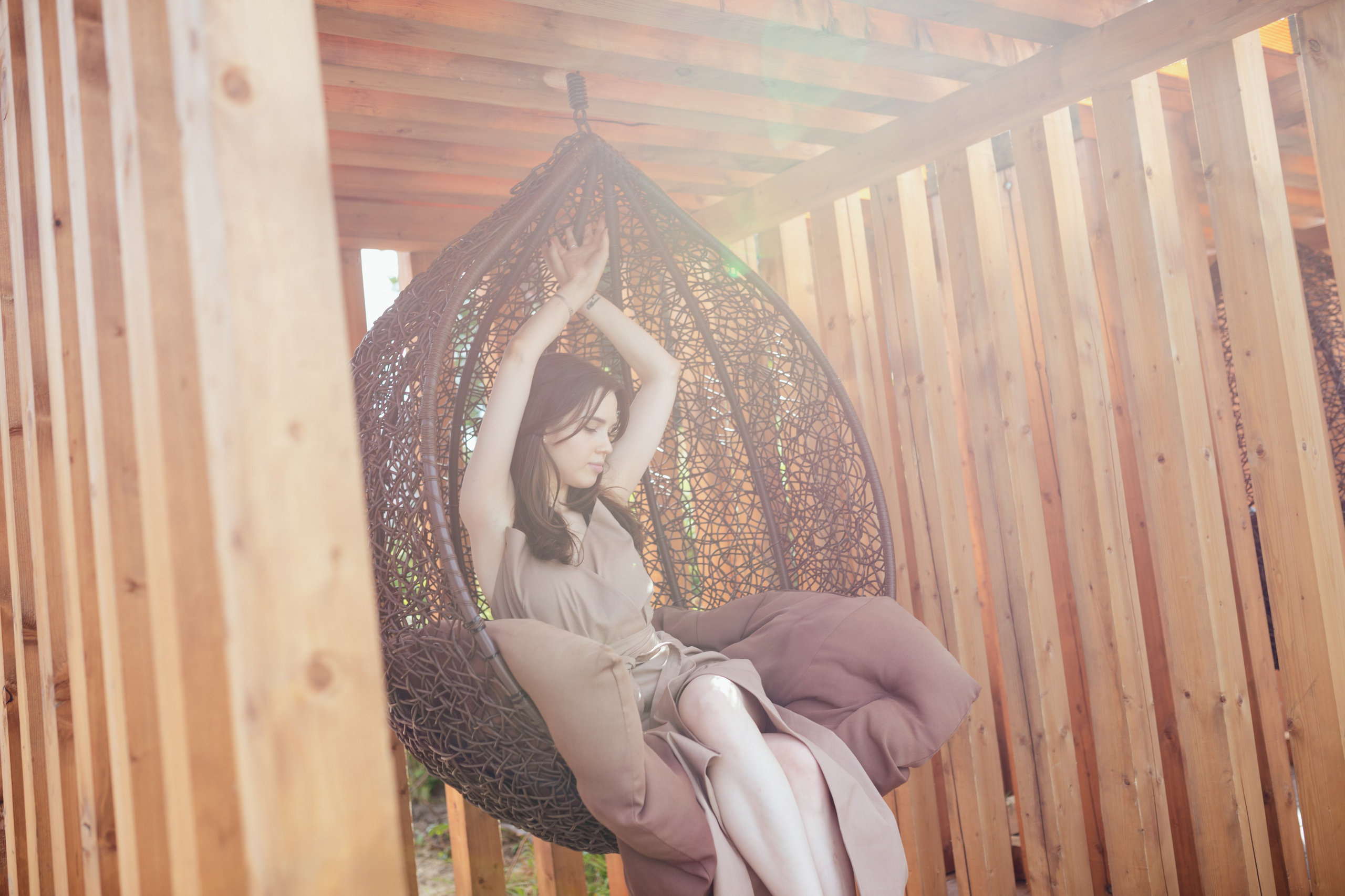 девушка в сидит в круглом соломенном кресле в лучах солнца