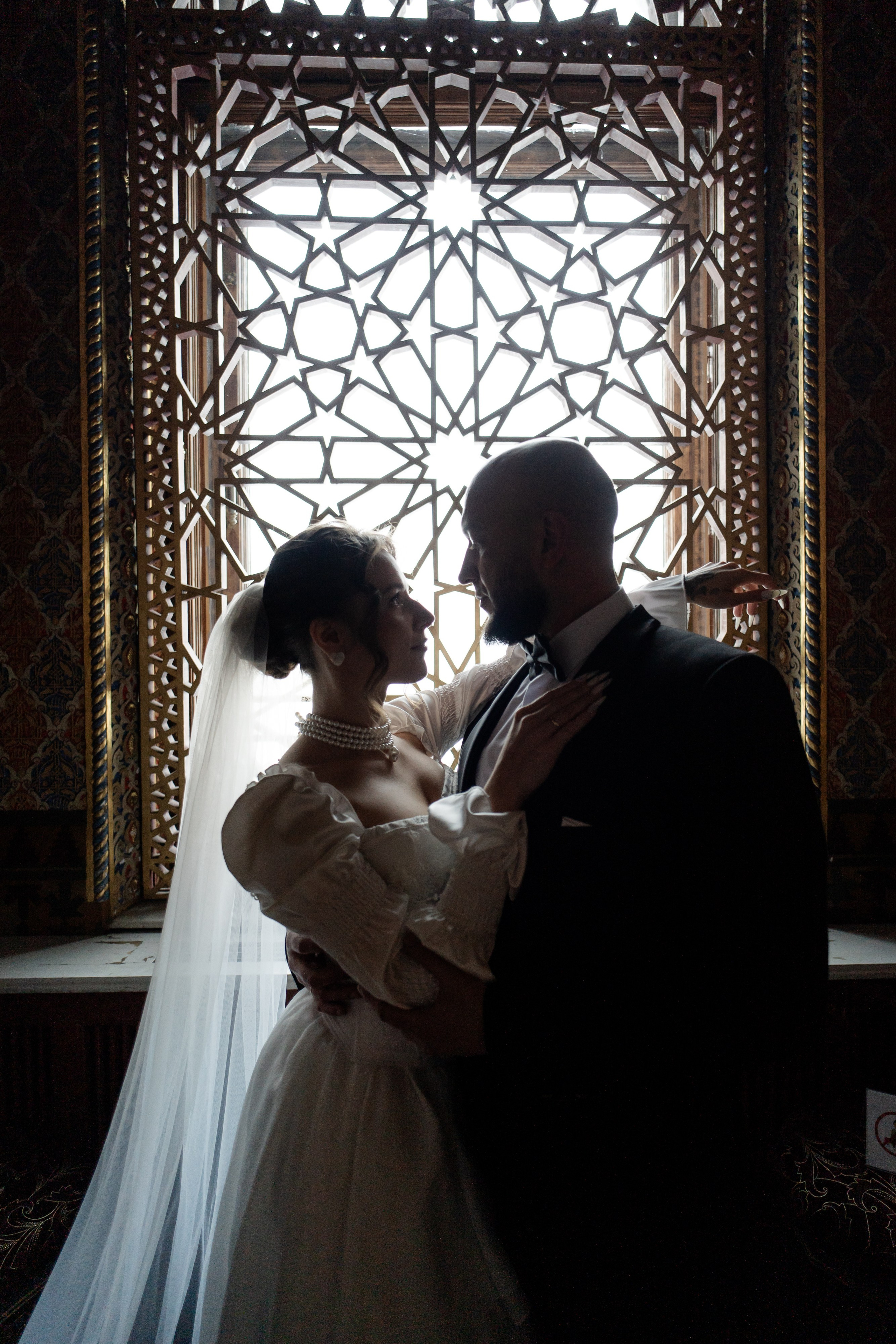 Невеста и жених красиво обнимаются у окна в иорданской гостиной