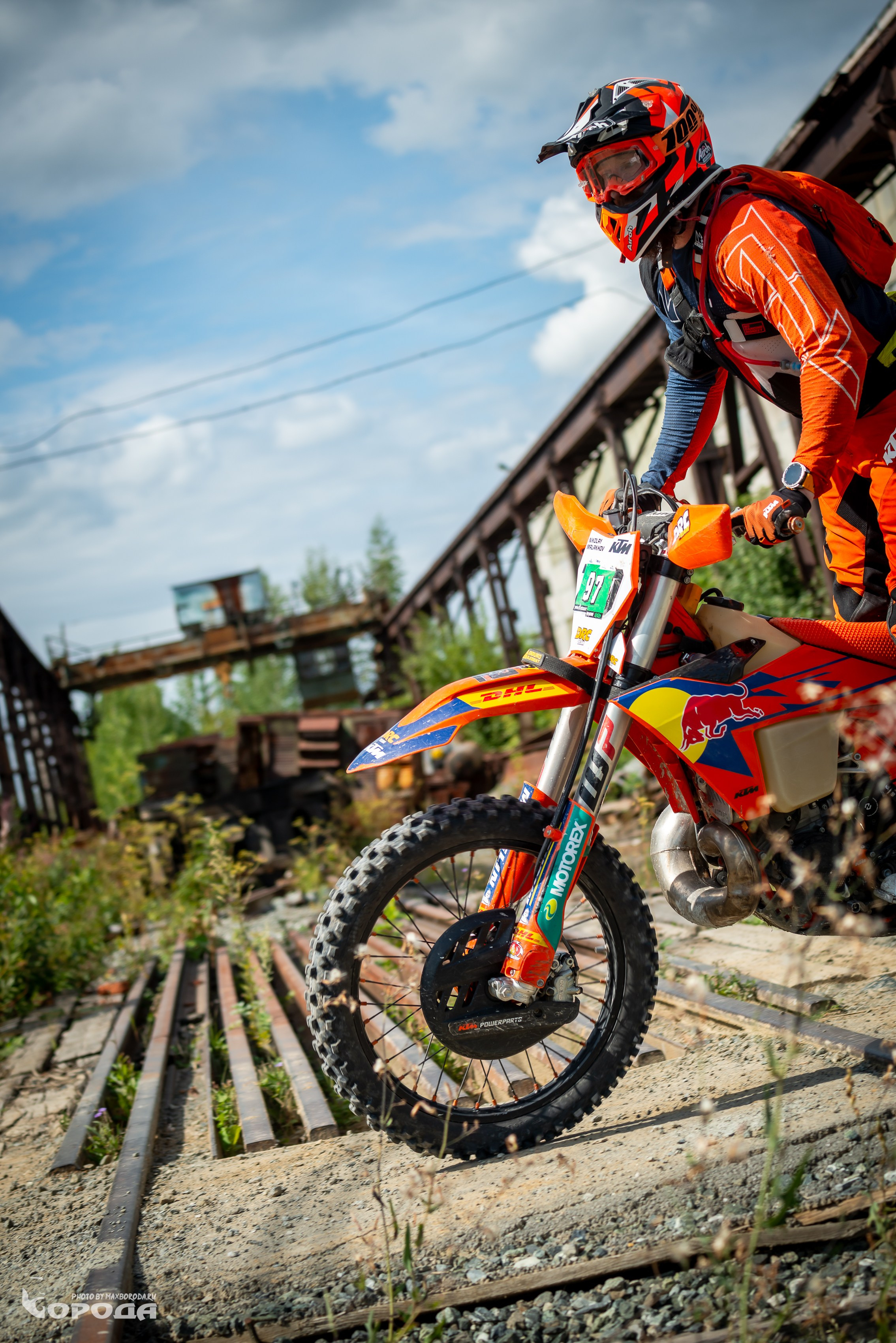 Мотокроссмен в оранжевой экипировке на KTM с логотипом Red Bull на заброшенной ветке.