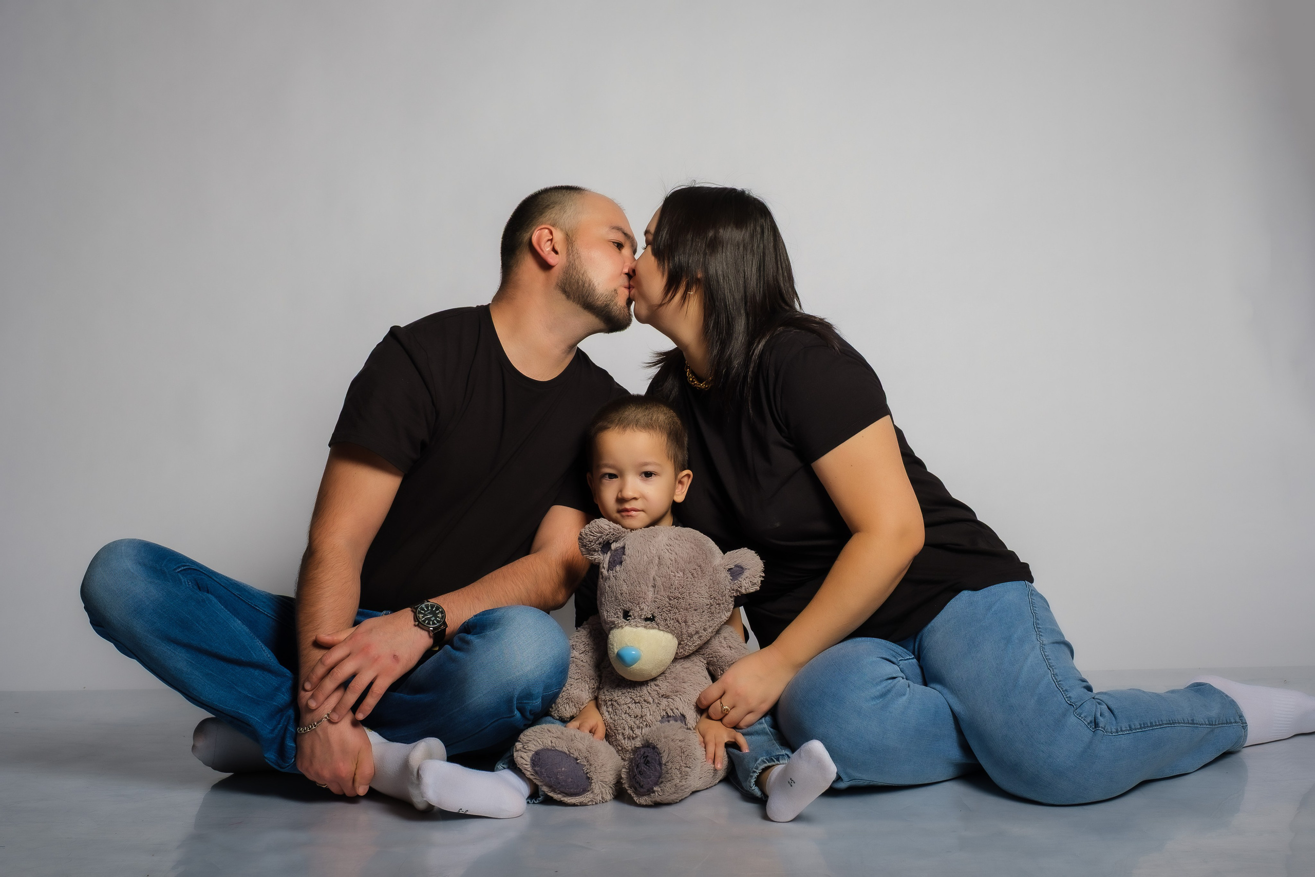 Ребёнок с игрушкой и рядом с ним его мать и отец целуют друг друга