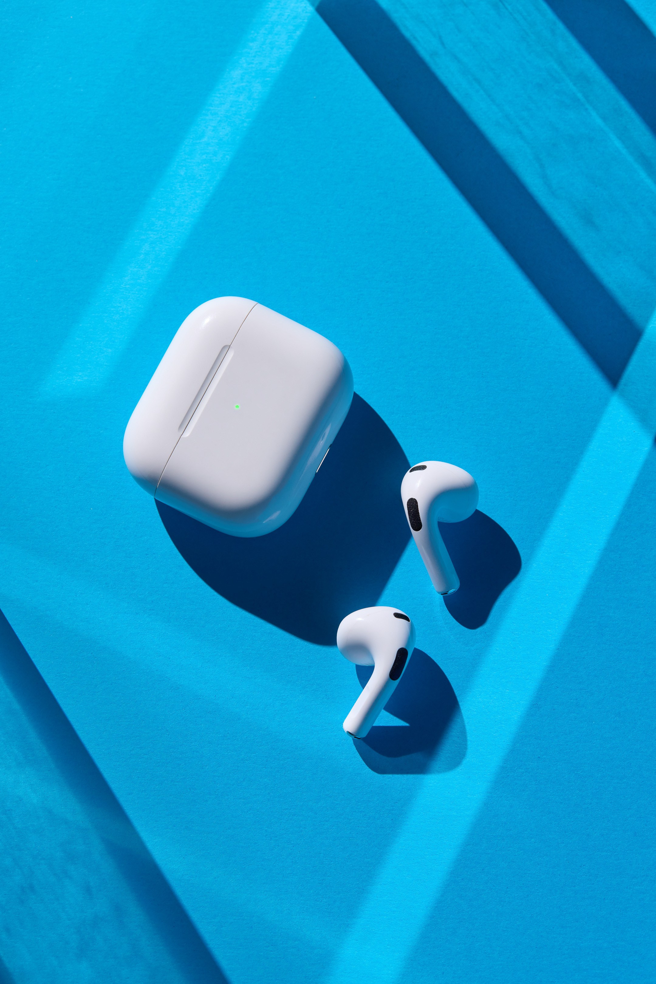 Apple AirPods on blue background with light rays and contrast shadows - photographer Andrey Dunin