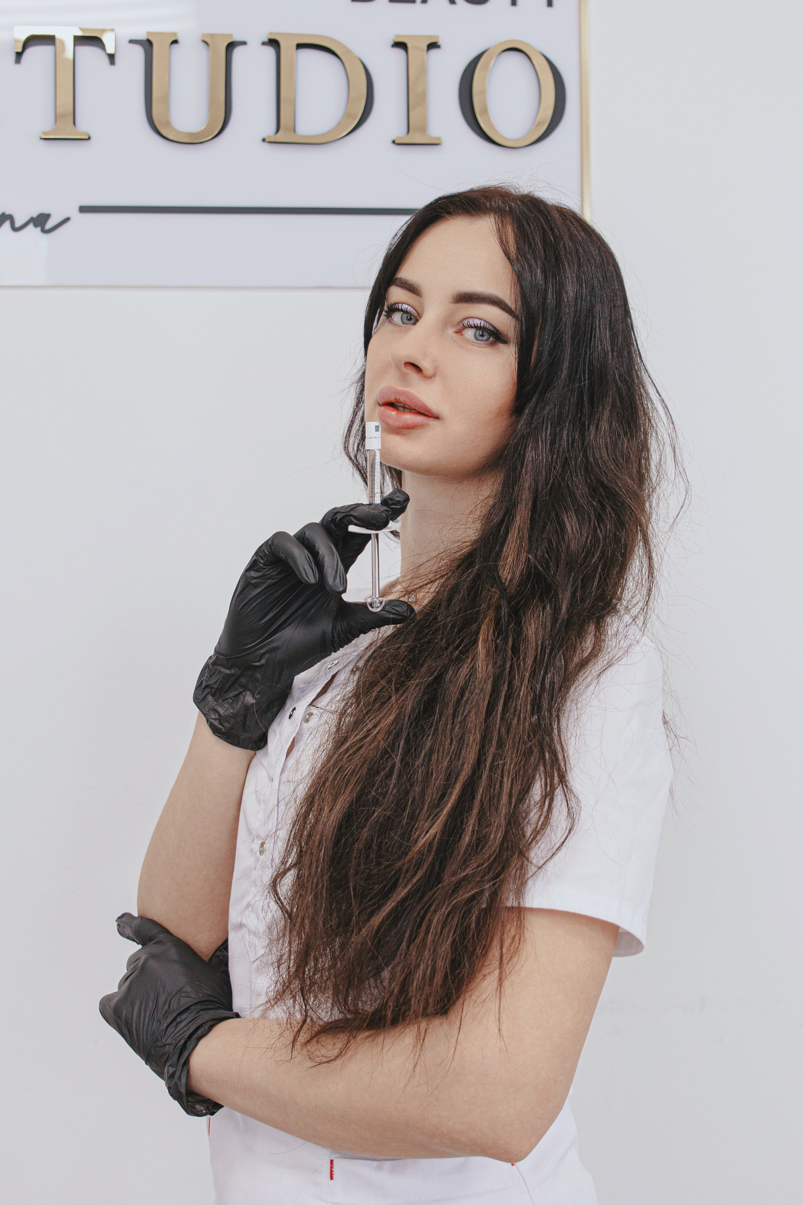 Косметолог улыбается, демонстрируя шприц с гиалуроновой кислотой для контурной пластики