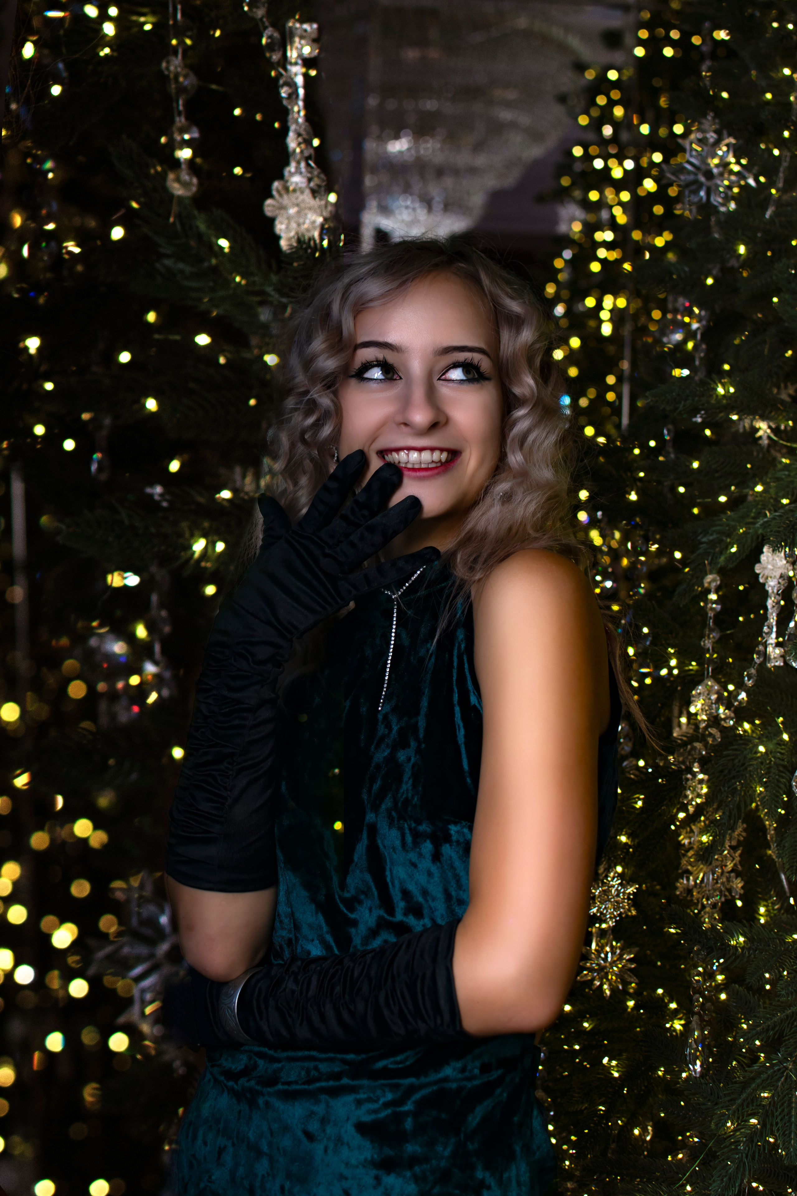 Девушка у ёлки смеется, прикрыв лицо ручкой в перчатке