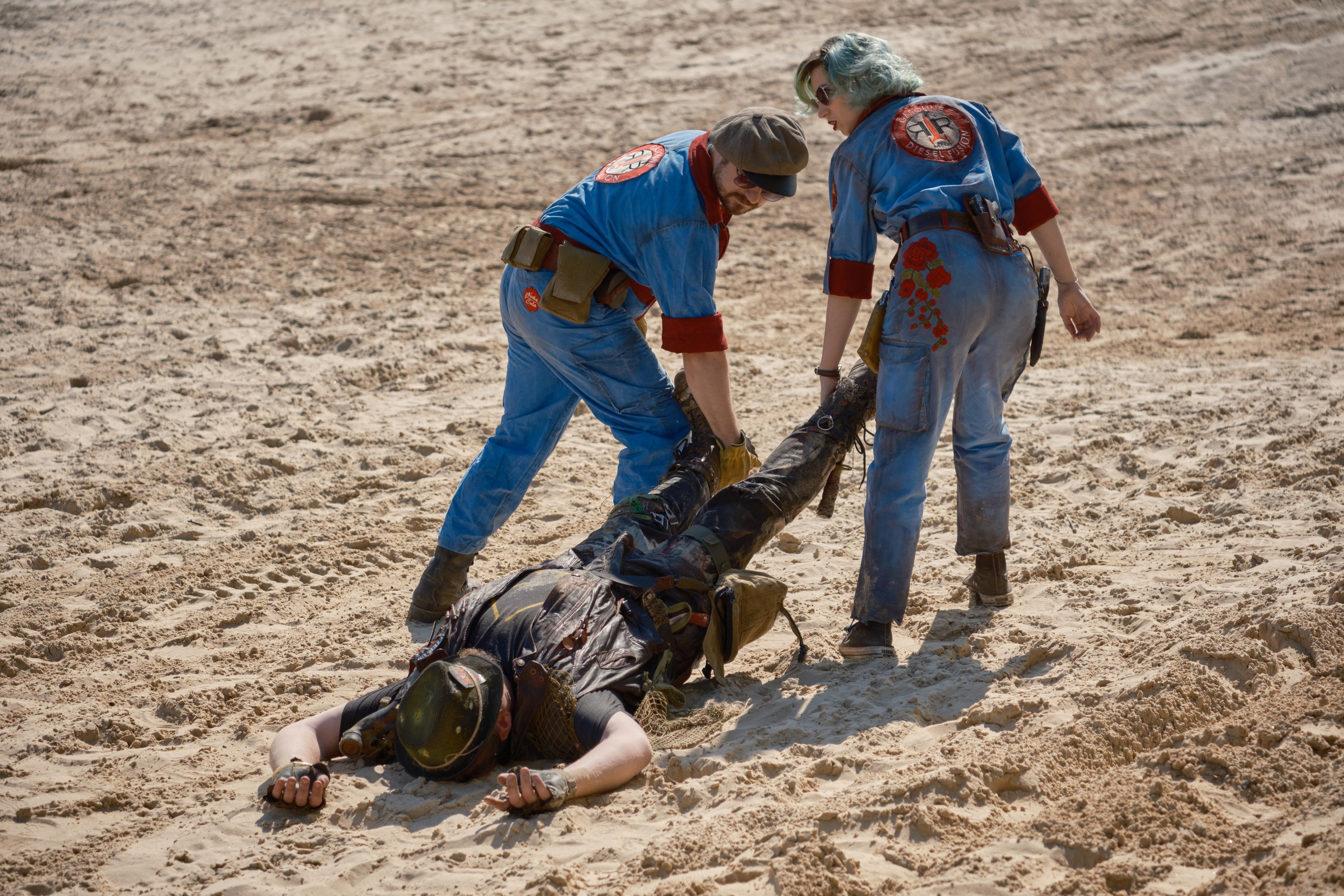 Девушка и мужчина в костюме выживших из Fallout. тащат труп по песку