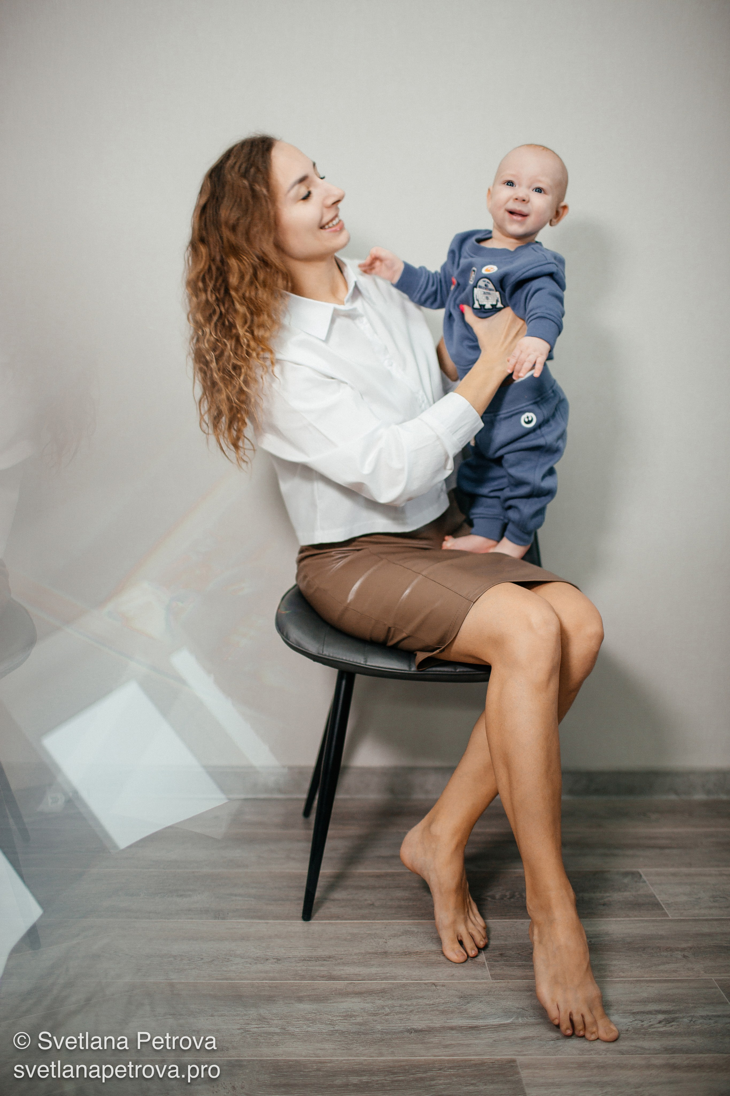 Мама с малышом на коленях — тёплая студийная съёмка. Улыбка мамы и смех ребёнка — семейный кадр. Мама держит малыша, радостная атмосфера. Малыш в голубом костюме на руках у мамы. Мама и ребёнок — искренний момент в кадре. Семейная фотосессия: мама с крохой дома. Радость в глазах малыша — мама рядом, уют.